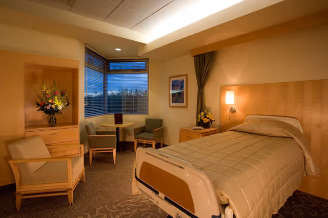 Hospital-style patient room with bed, seating area, and window