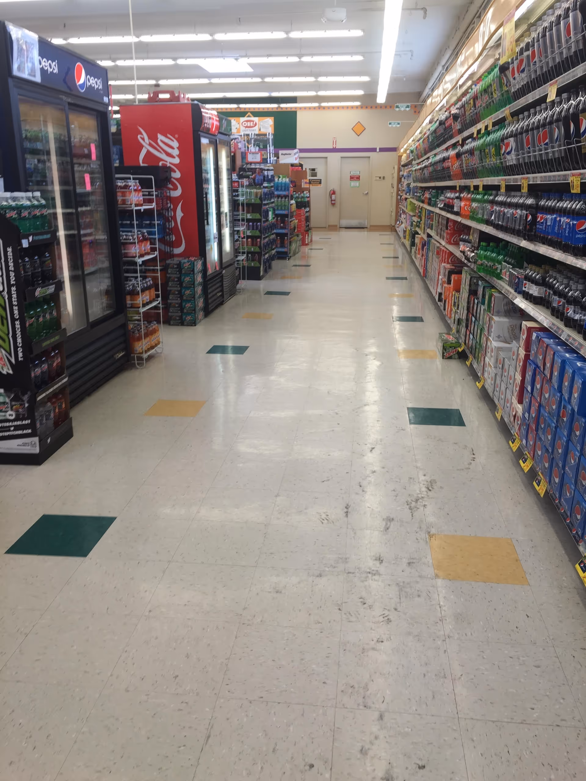 Long grocery store aisle with beverage refrigerators on left and soda displays on right.