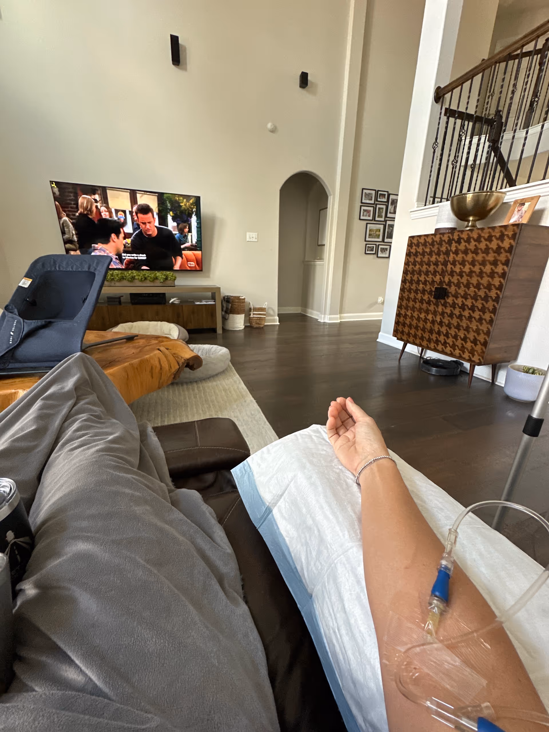 Resident reclining on a sofa in a modern living room with TV and IV line.