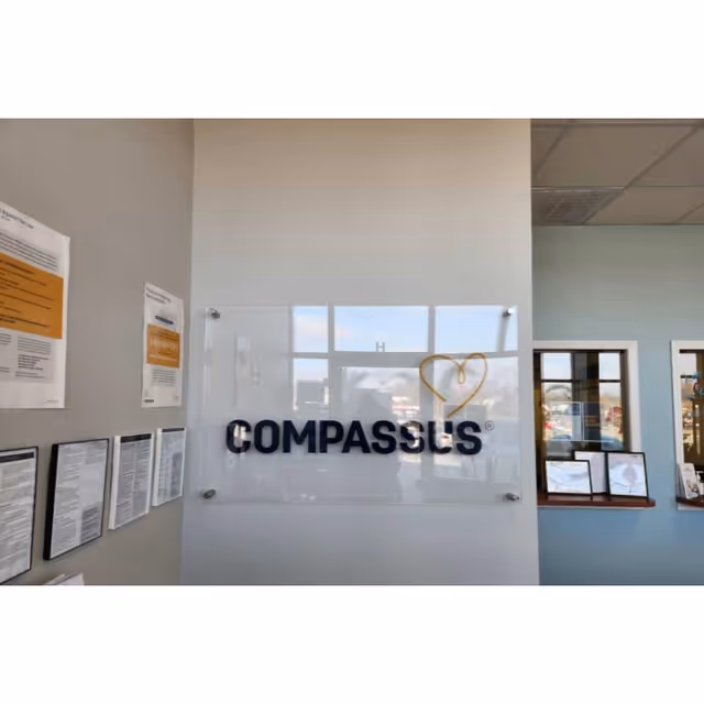 Interior lobby with a glass sign reading COMPASSUS and a heart logo.