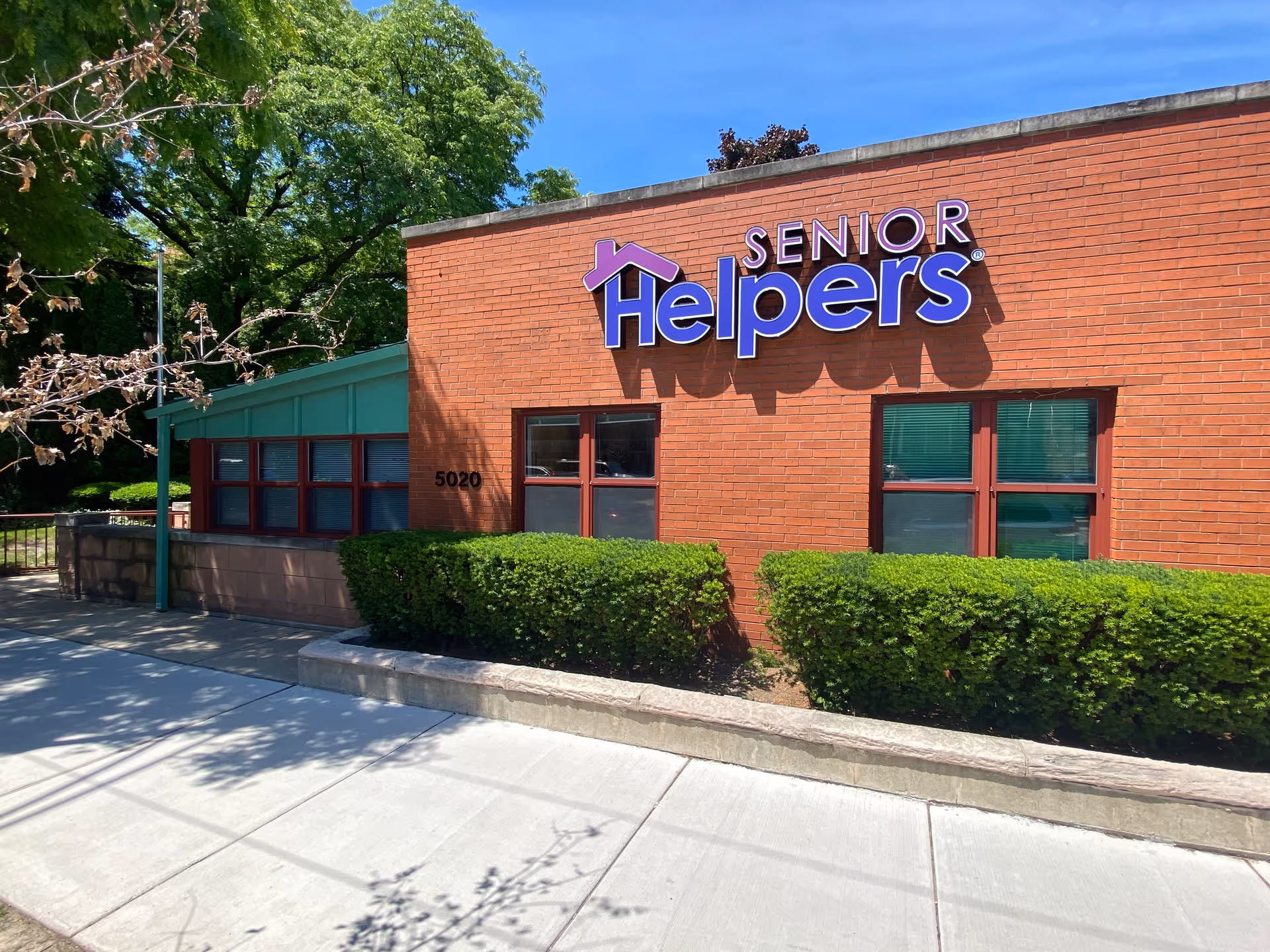 Brick Senior Helpers building exterior with sign, windows, and trimmed hedges.