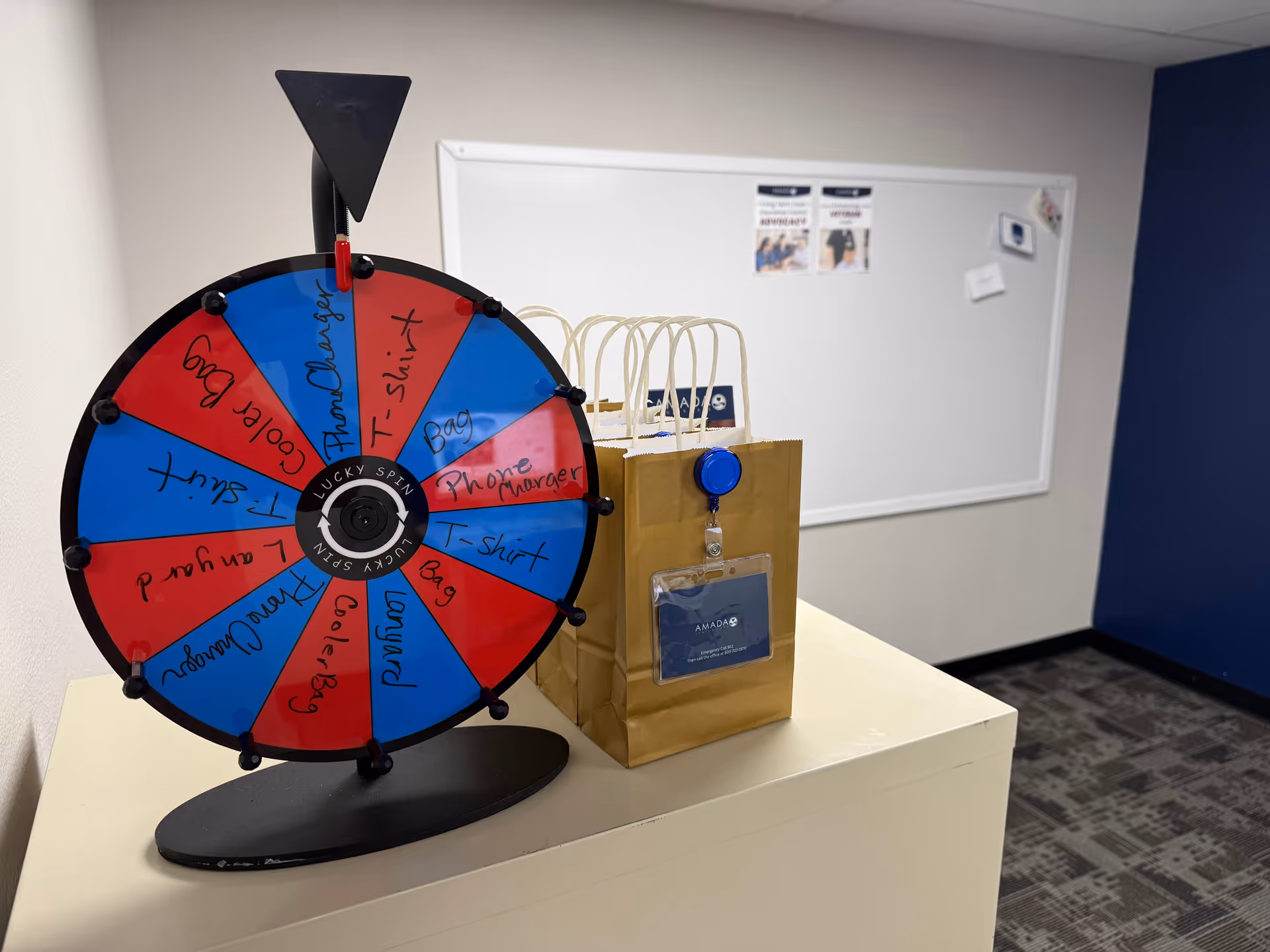 A colorful spinning prize wheel and gift bag sit on a white counter indoors.