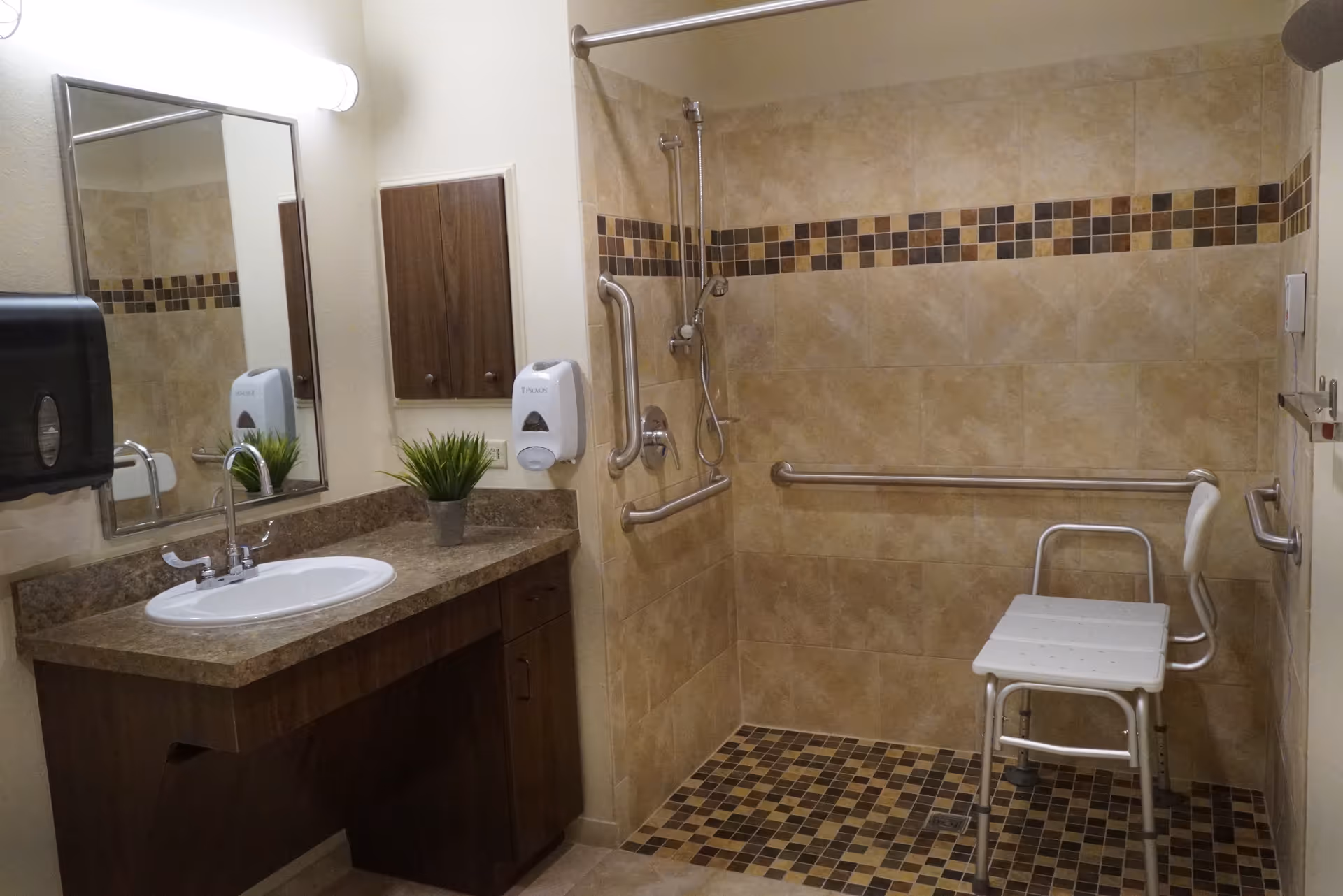 Accessible senior bathroom with sink, mirror, grab bars, and a shower chair.