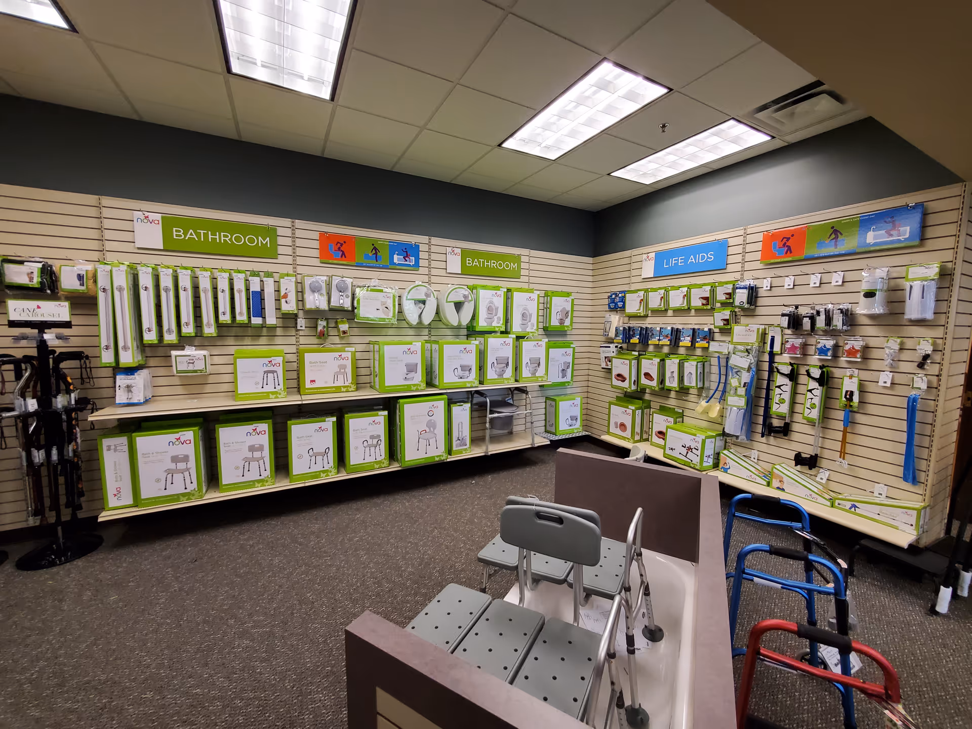 Inside a store-like facility, wall shelves display bathroom and life aid products with walkers in front.