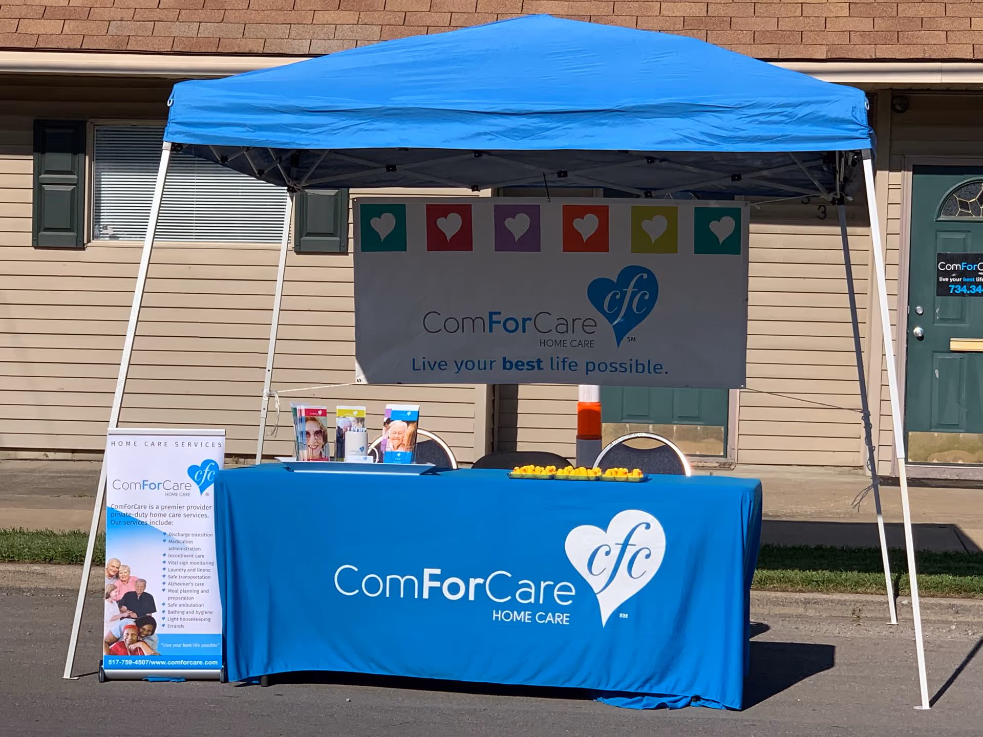 Outdoor promotional booth with blue canopy and ComForCare banner outside a building.