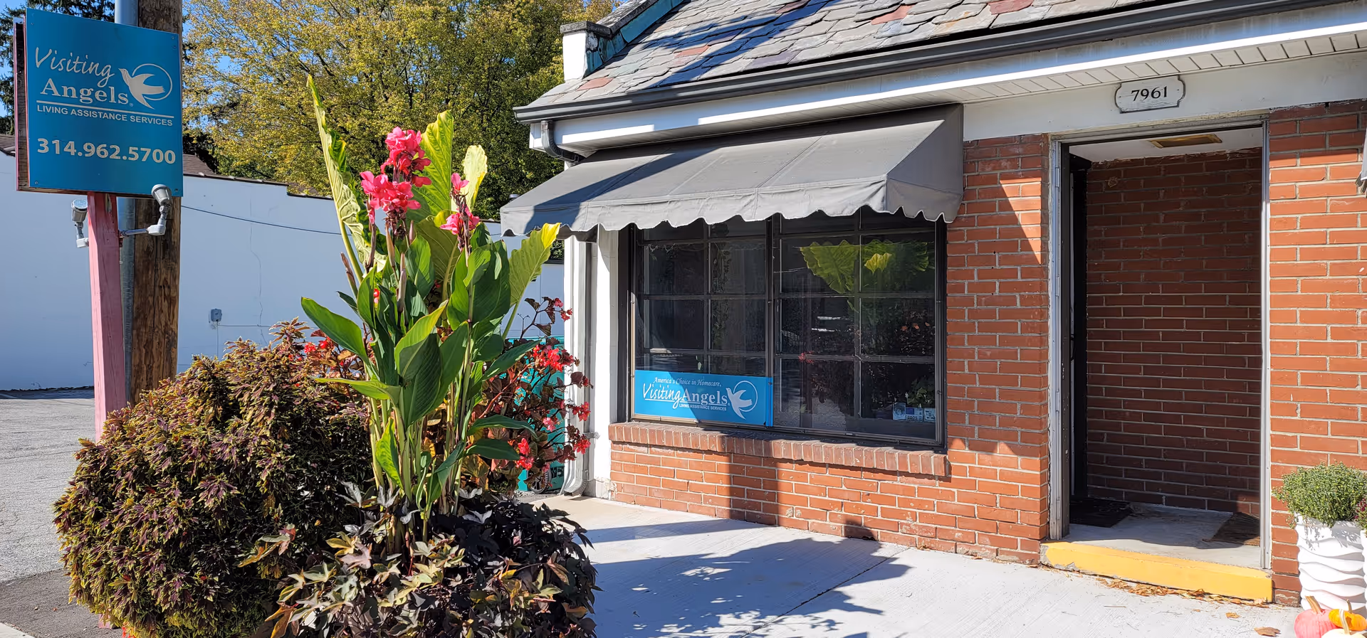 Brick storefront with awning, Visiting Angels sign, front entrance, and vibrant plants.