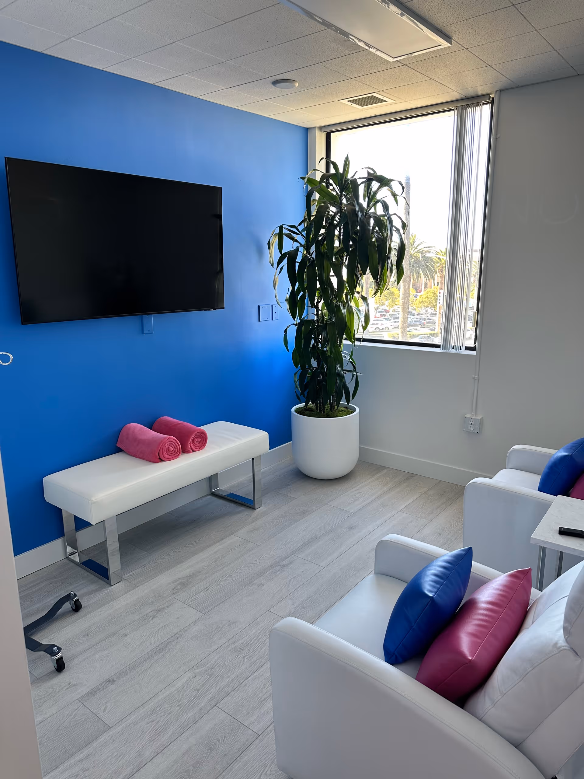 Bright lounge in a senior facility with blue wall, TV, and white seating.