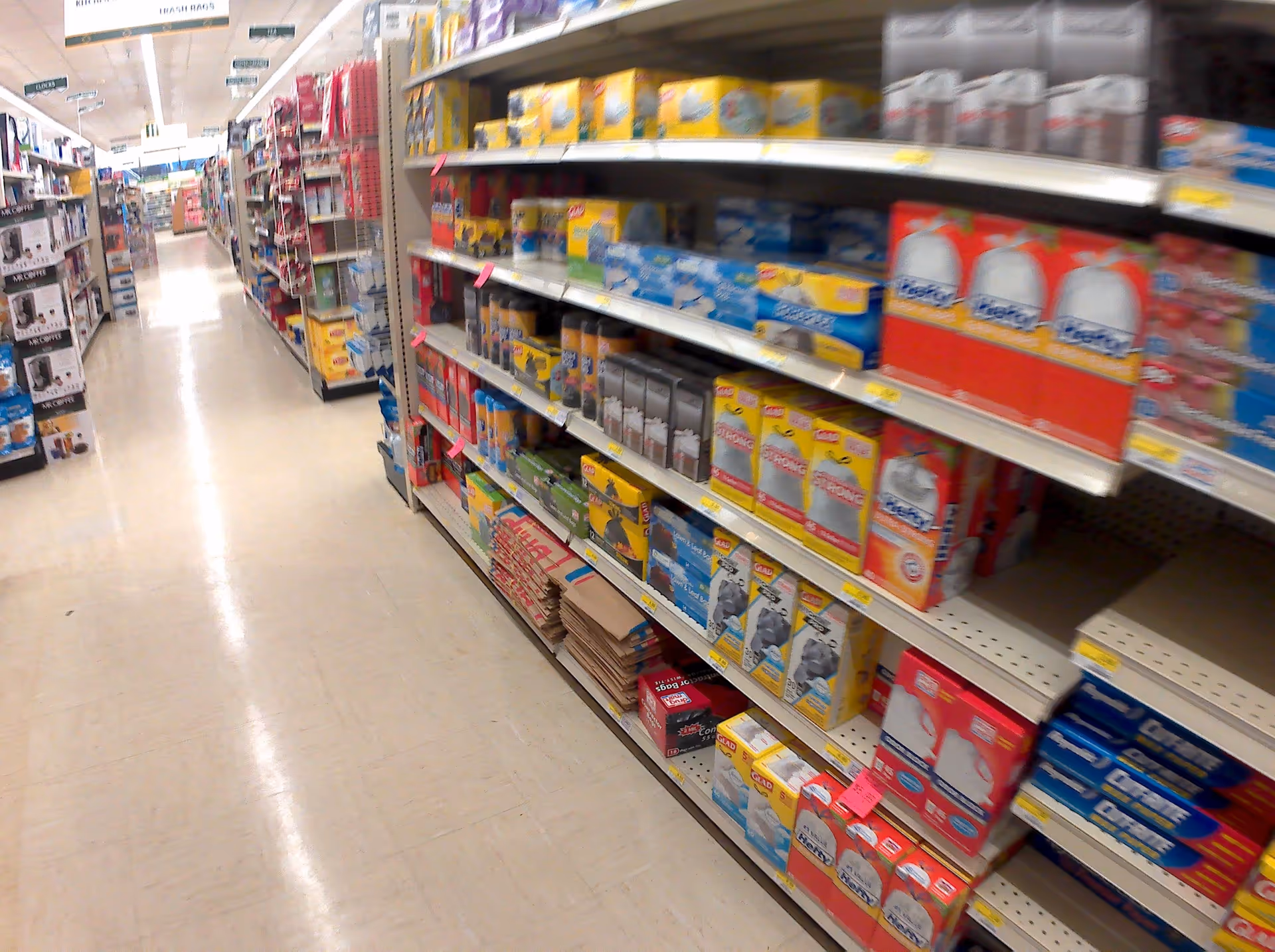 A wide supermarket aisle with shelves of groceries and household items.