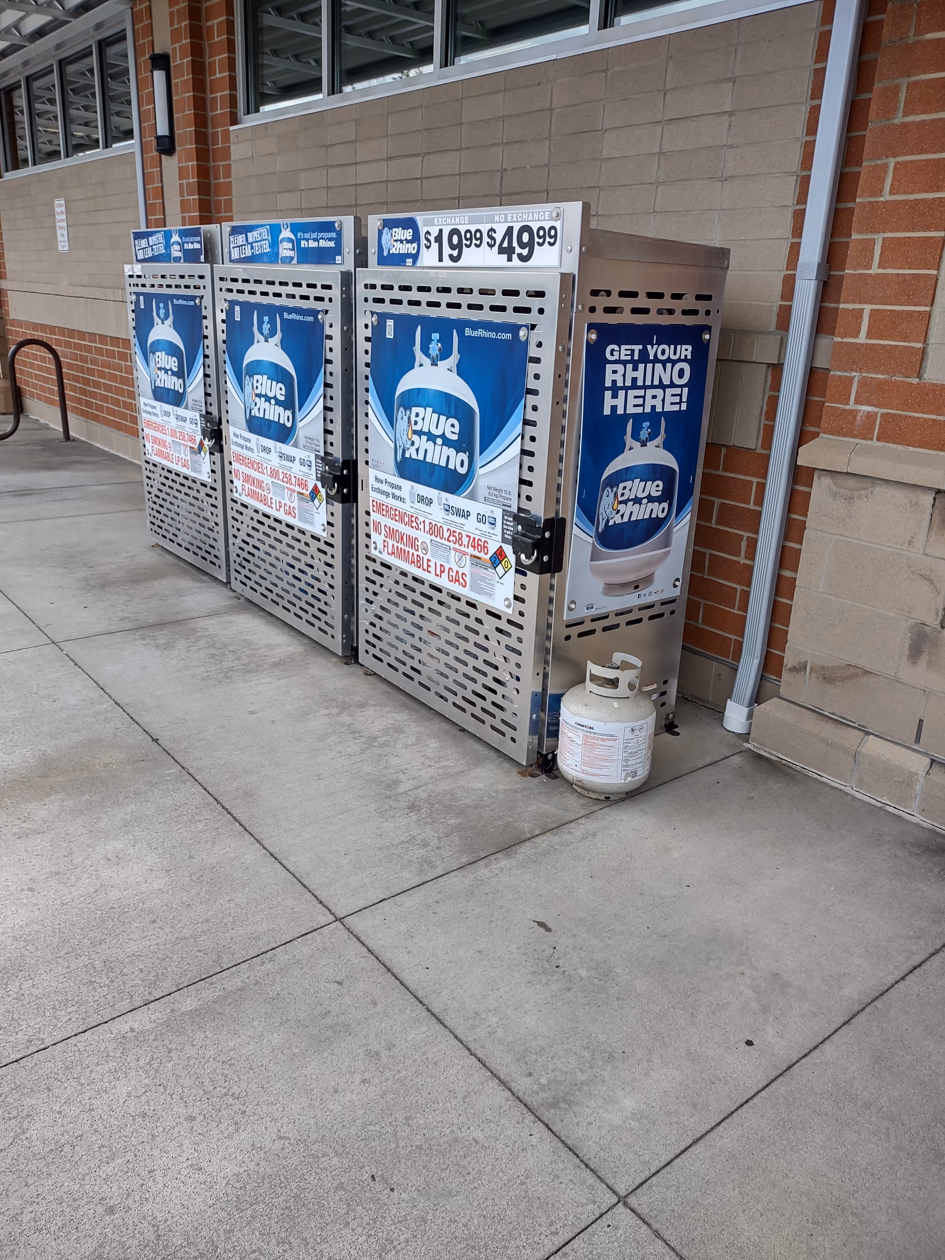 Outdoor view of Blue Rhino propane tank exchange cages outside a brick building.