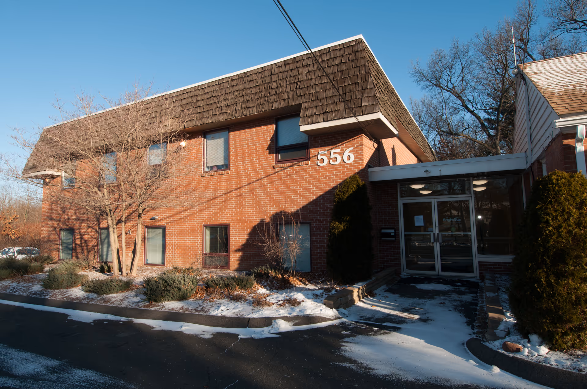 Brick senior living facility exterior with glass entrance and snow along the walkway.