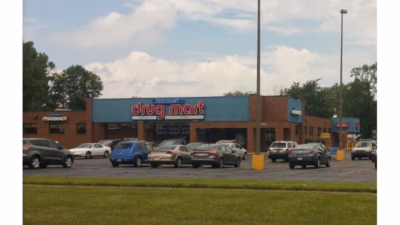 Exterior view of a Discount Drug Mart storefront with a parking lot and cars.