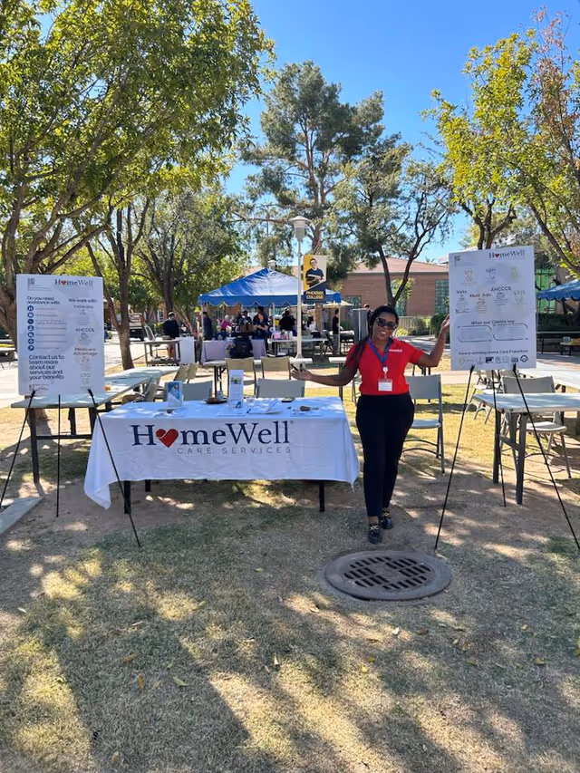 Outdoor HomeWell Care Services booth with staff member among tents and trees