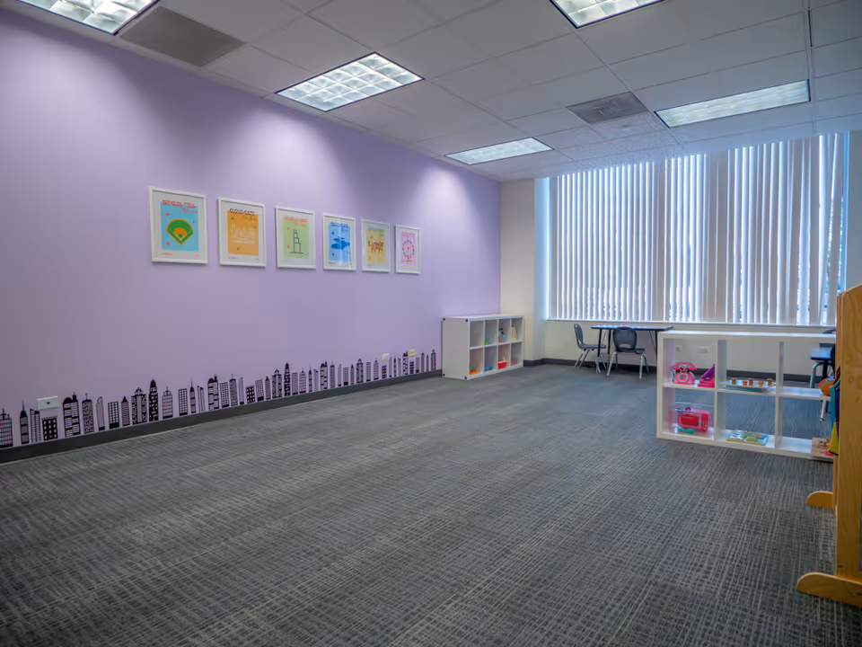 Spacious interior activity room with purple wall, framed art, shelves, and large window blinds