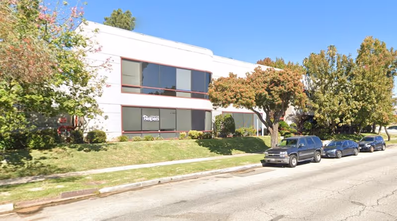 Exterior view of a Senior Helpers building along a street with parked cars and trees.