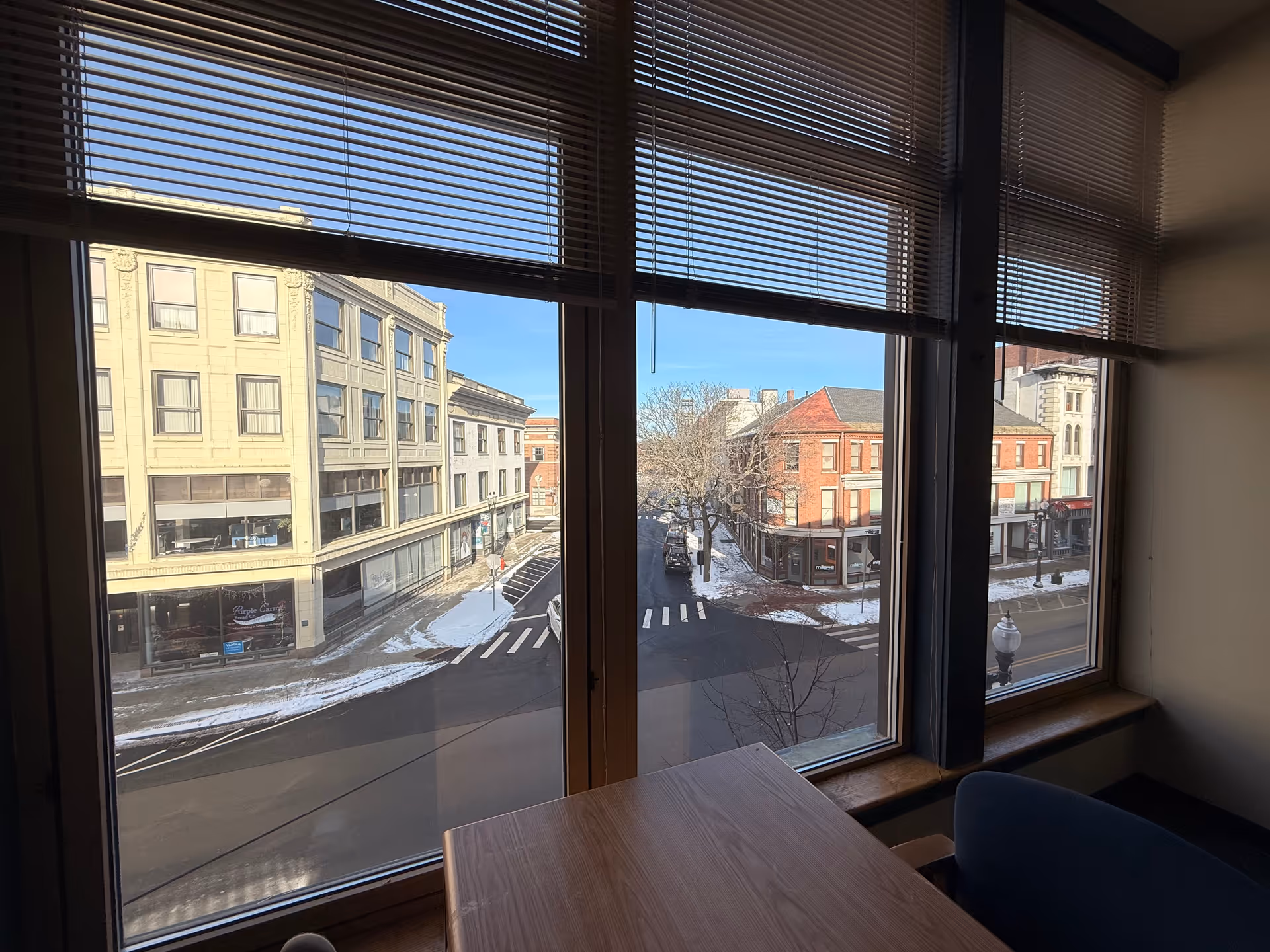Inside a room with large windows and a wooden table overlooking a snowy street.