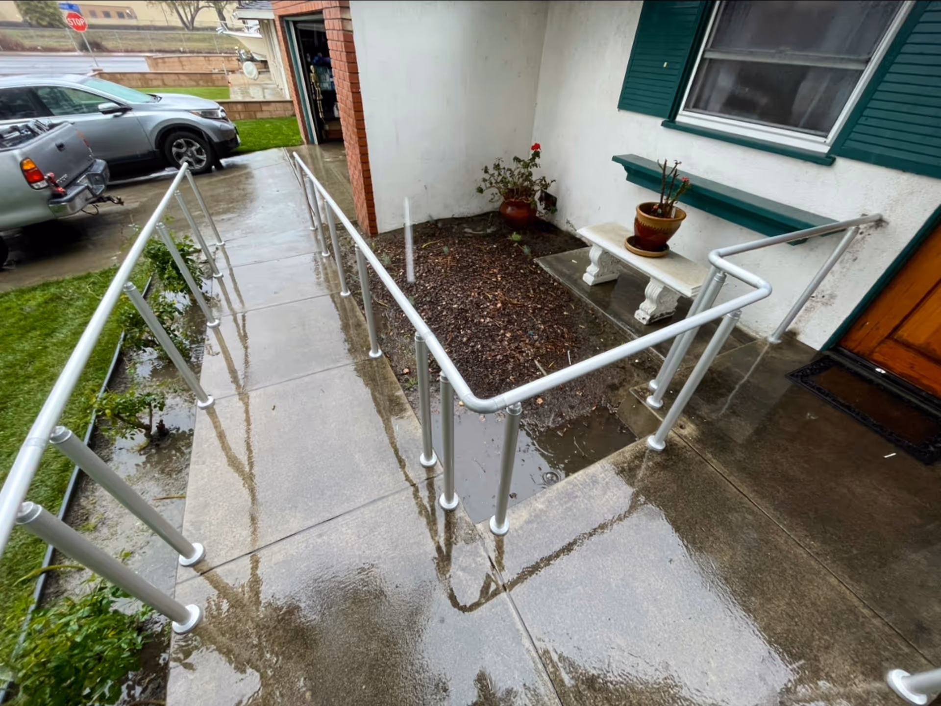 Wet concrete entry ramp with metal handrails leading to a doorway.