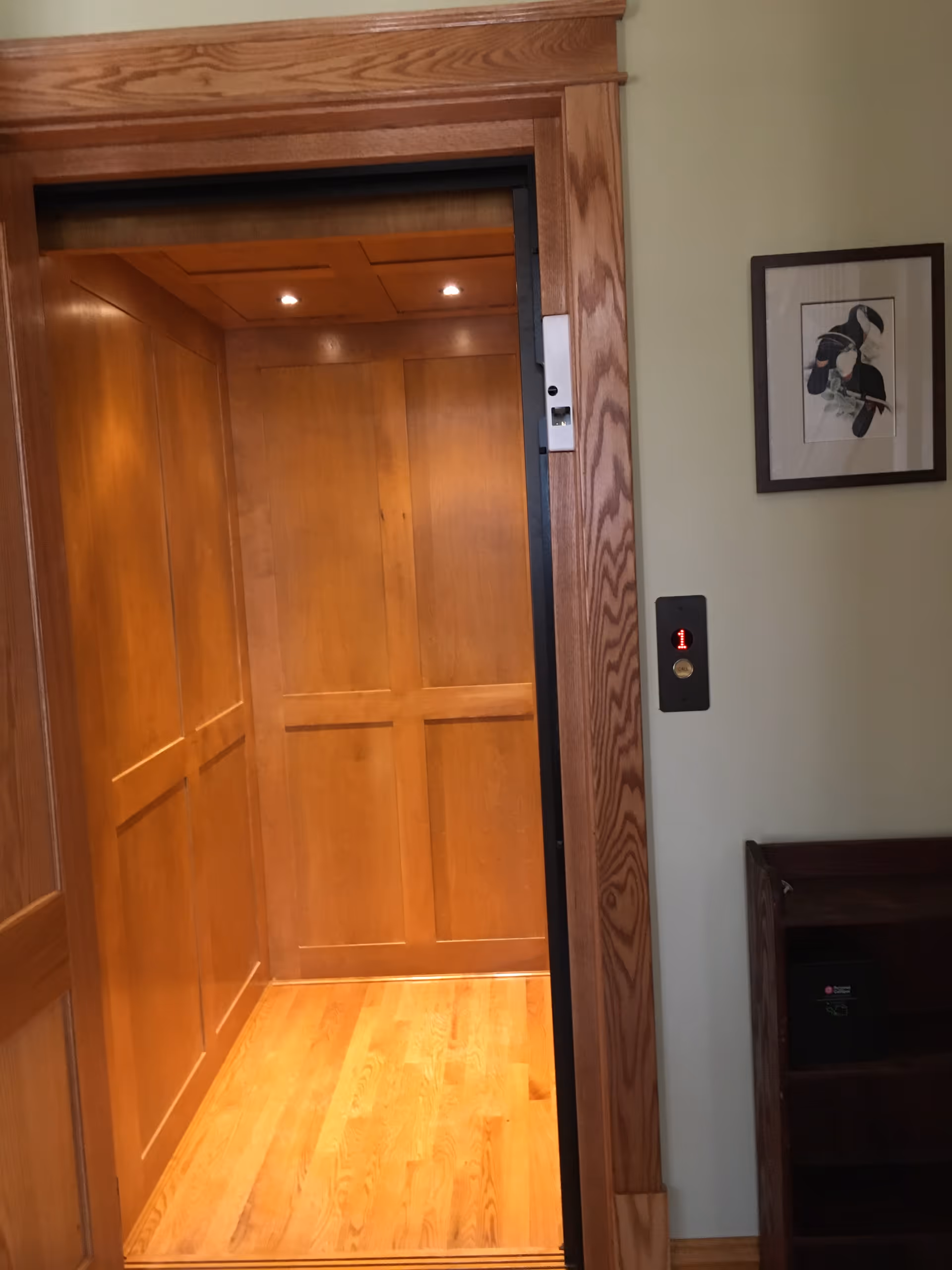 Wood-paneled elevator interior with framed artwork on a green wall.