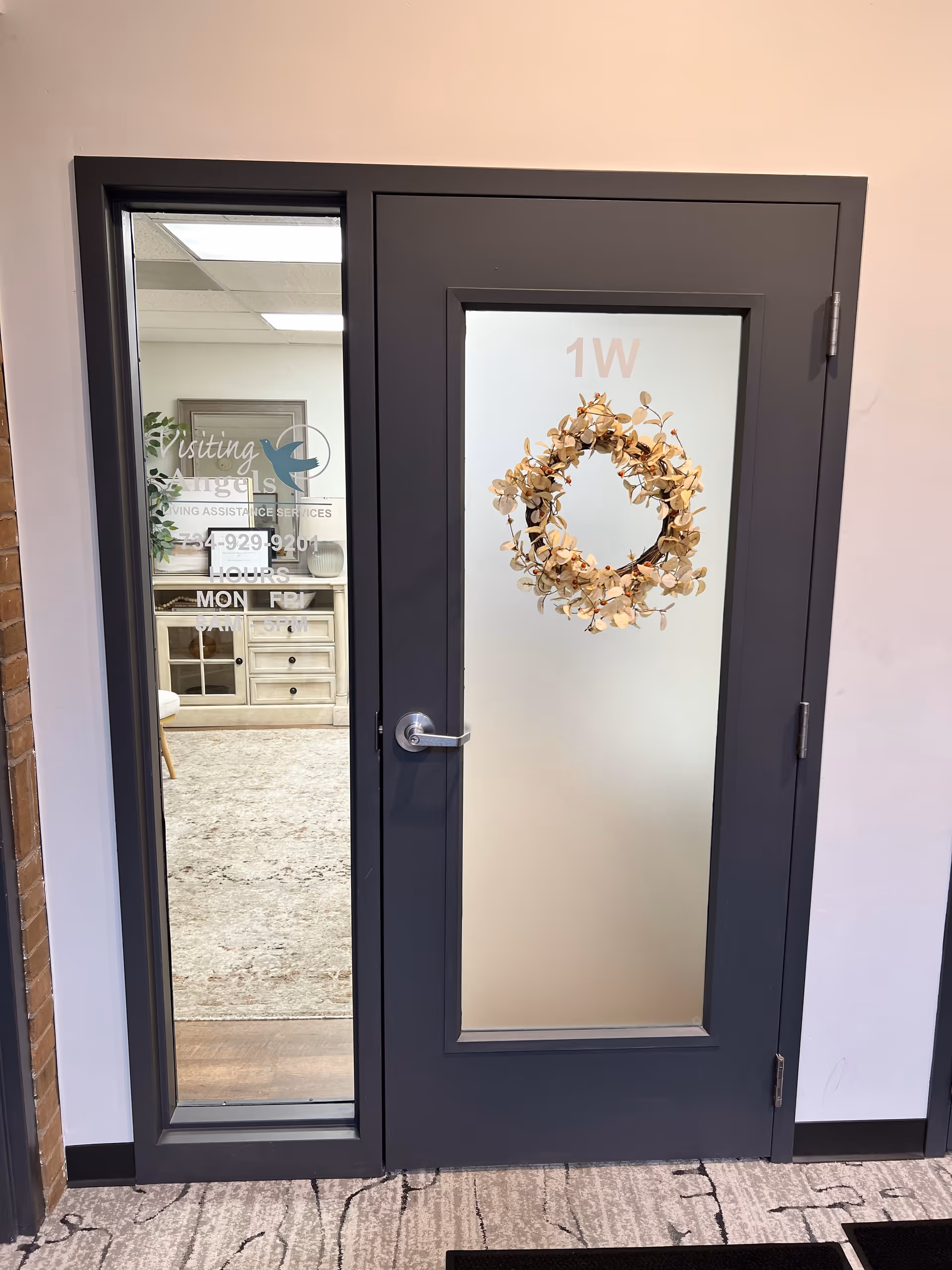 Dark-framed interior door with frosted glass and wreath, adjacent panel shows office interior.