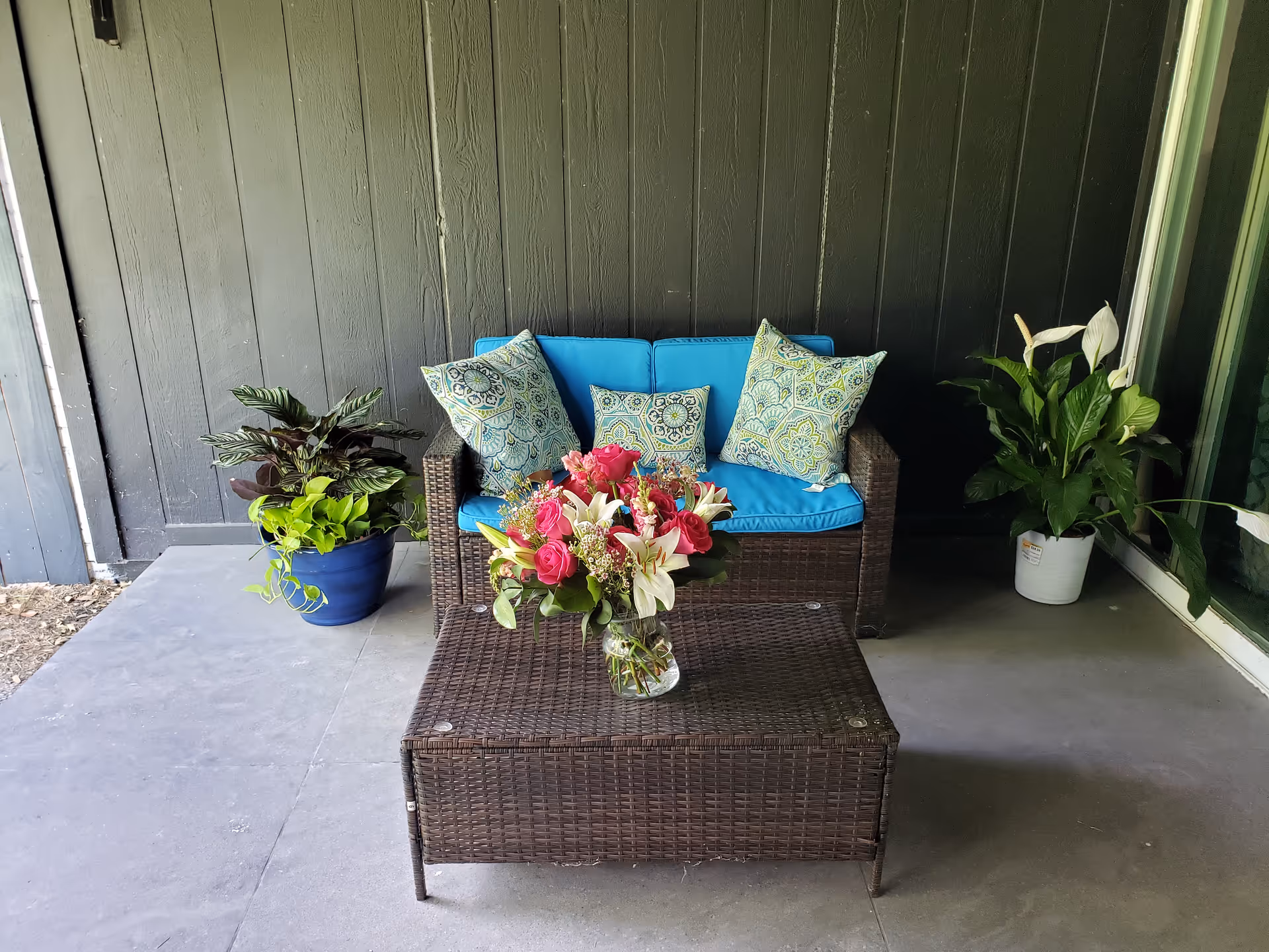 Outdoor patio with wicker sofa, blue cushions, coffee table, and potted plants.