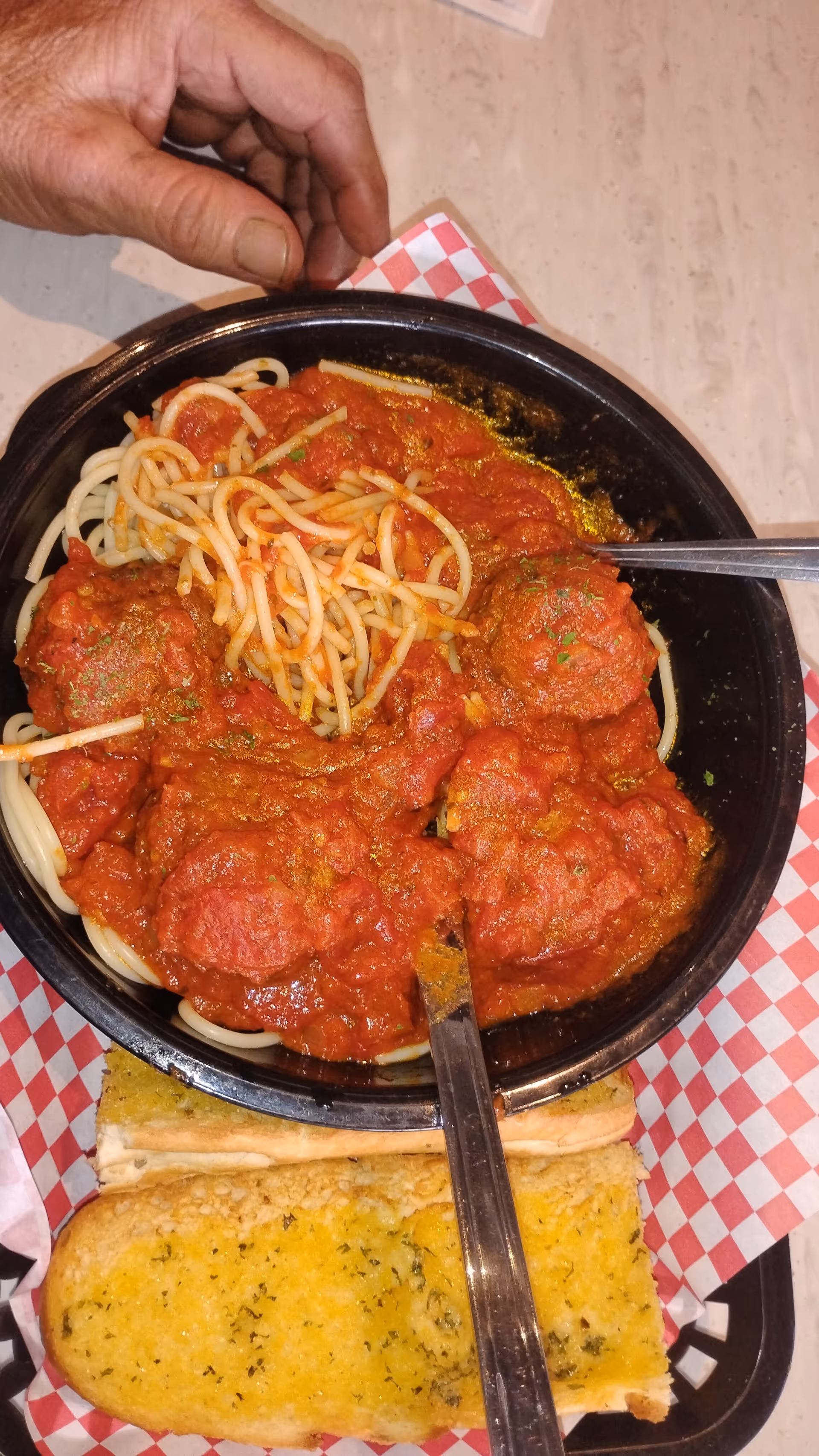 A hand reaches toward a bowl of spaghetti with marinara sauce and garlic bread on table.