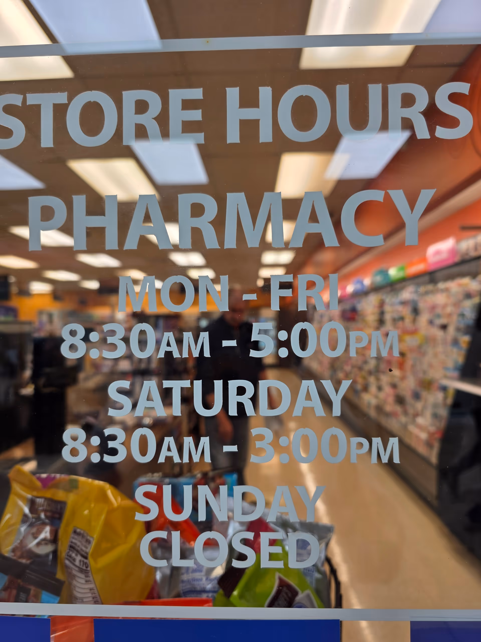 Glass storefront shows Kroger Pharmacy hours with interior shelves visible through glass.