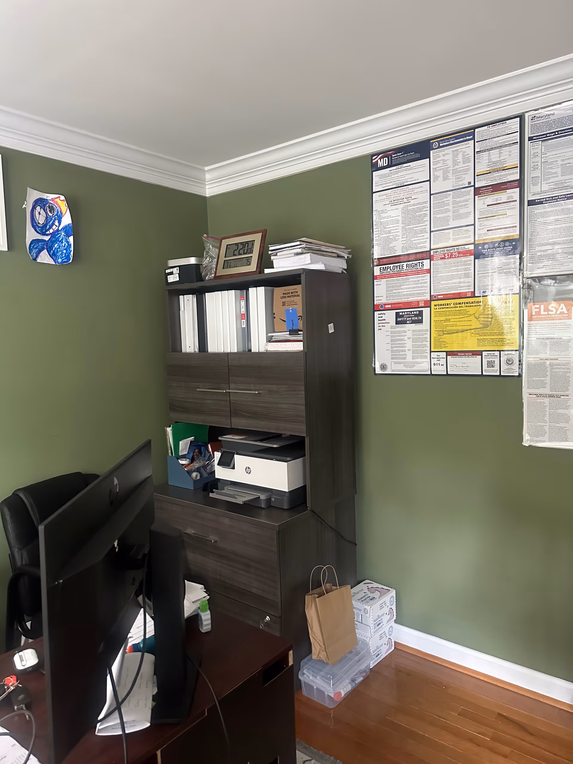 Office workspace with computer, printer, filing cabinet, and wall posters on green walls.