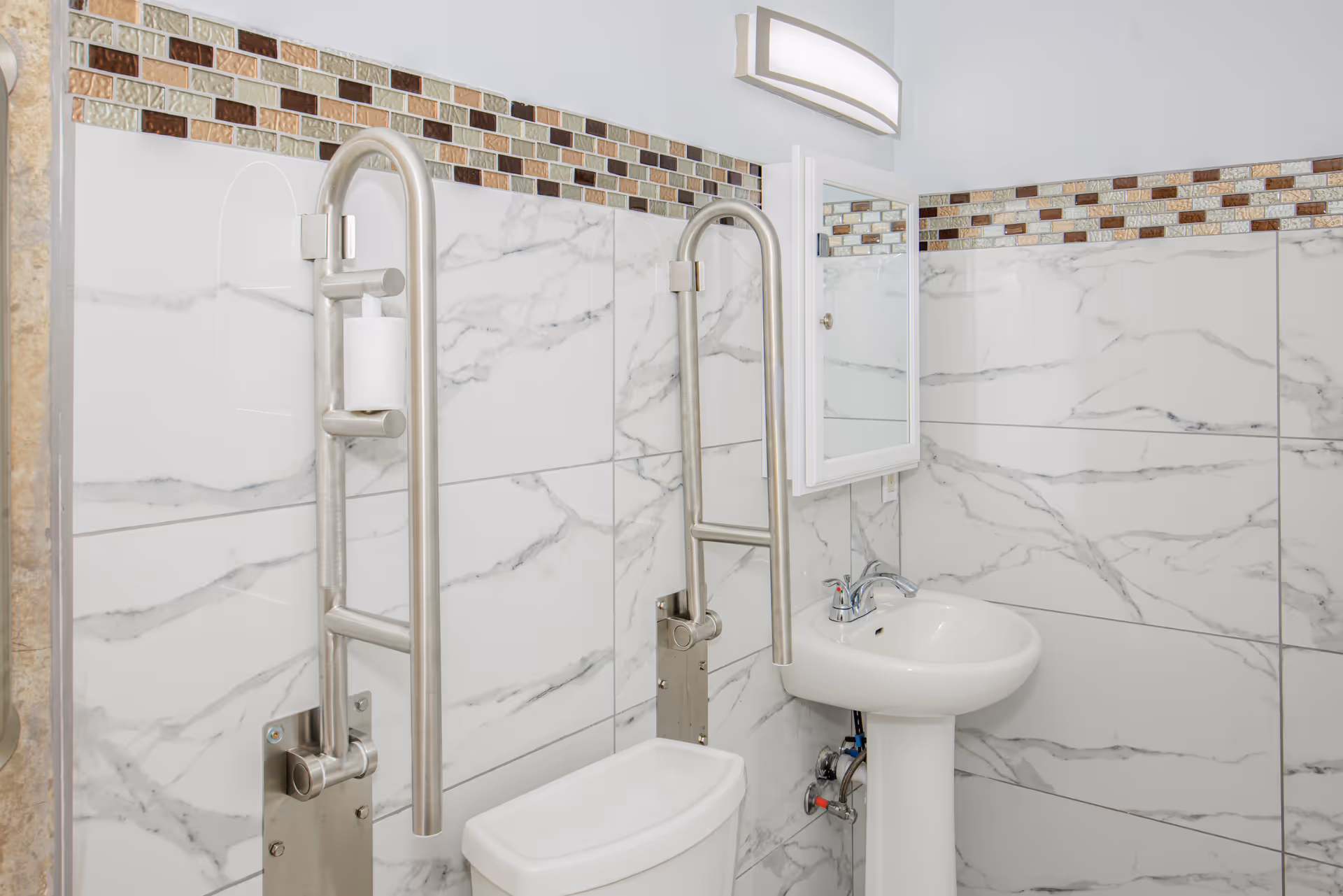 Accessible bathroom with grab bars, sink, and toilet tiled in marble pattern.