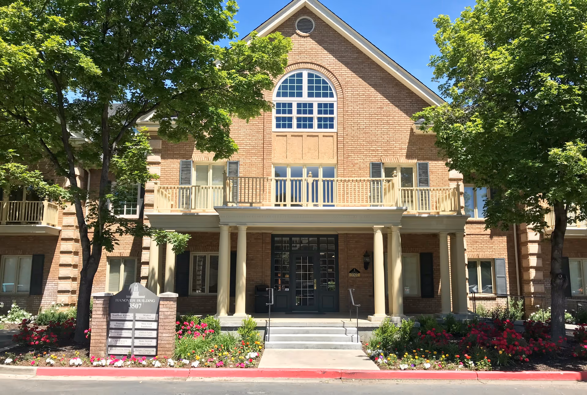 Brick senior living building with columns, balconies, and a landscaped entrance.