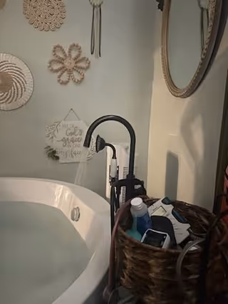 A bathroom with a corner tub, sink, mirror, and vanity basket of toiletries.