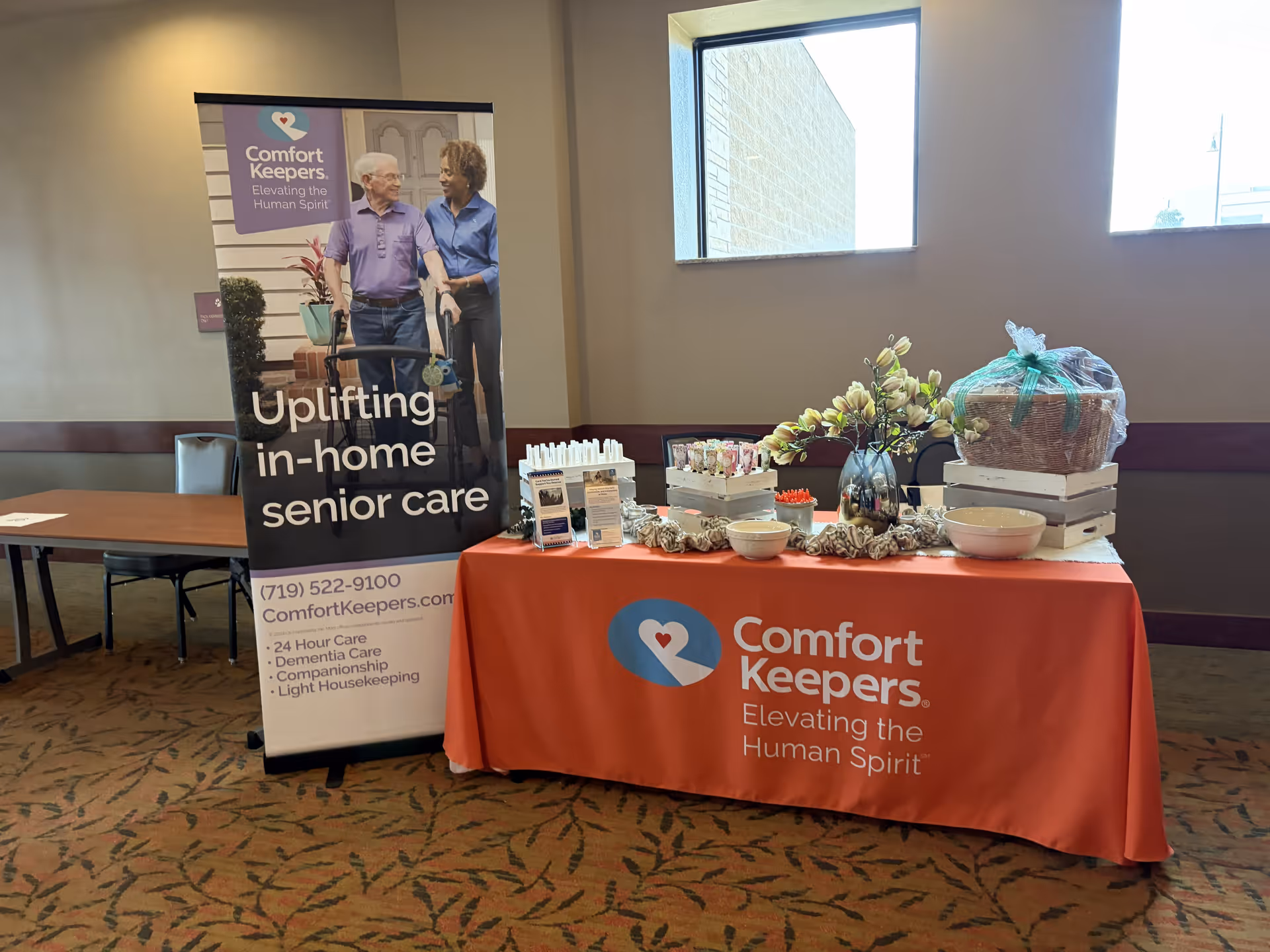 Indoor promotional booth for Comfort Keepers with banner and gift table.