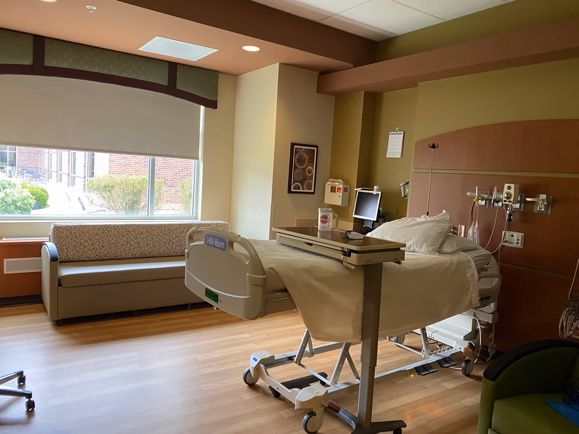 Interior patient room with hospital bed, medical equipment, and a couch near a window.