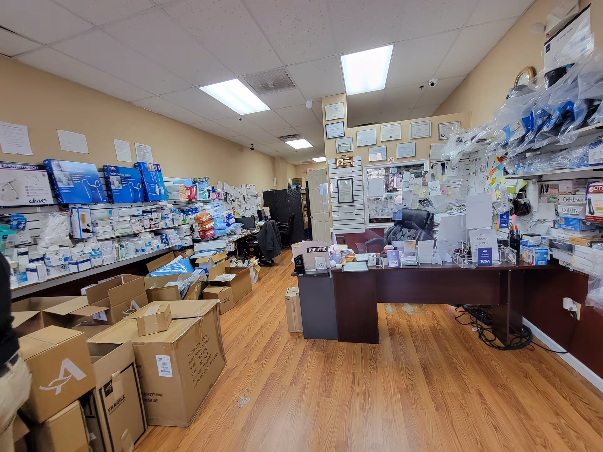 Cluttered interior supply room with medical boxes on shelves and a front desk.