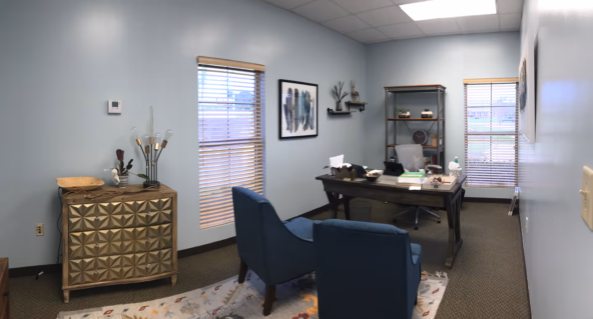 Small office space with a desk, chairs, shelves, and blue walls in a senior living interior.