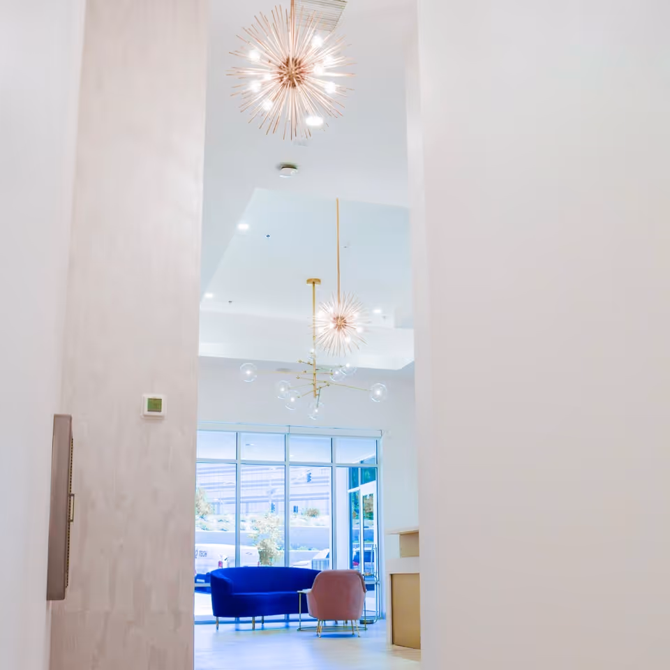 Bright modern lobby with large windows, hanging lights, and blue seating.