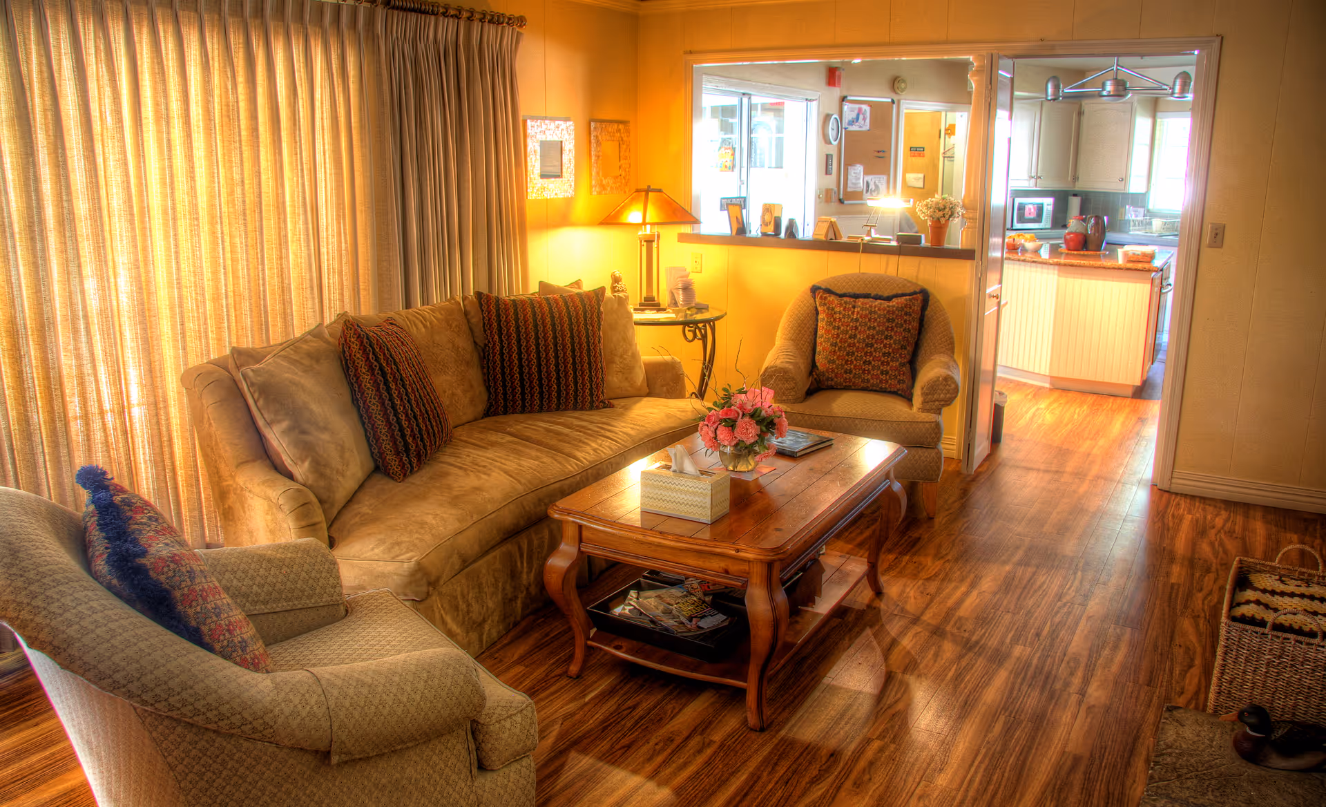 Cozy living room with sofa, chairs, coffee table, and kitchen visible through doorway.