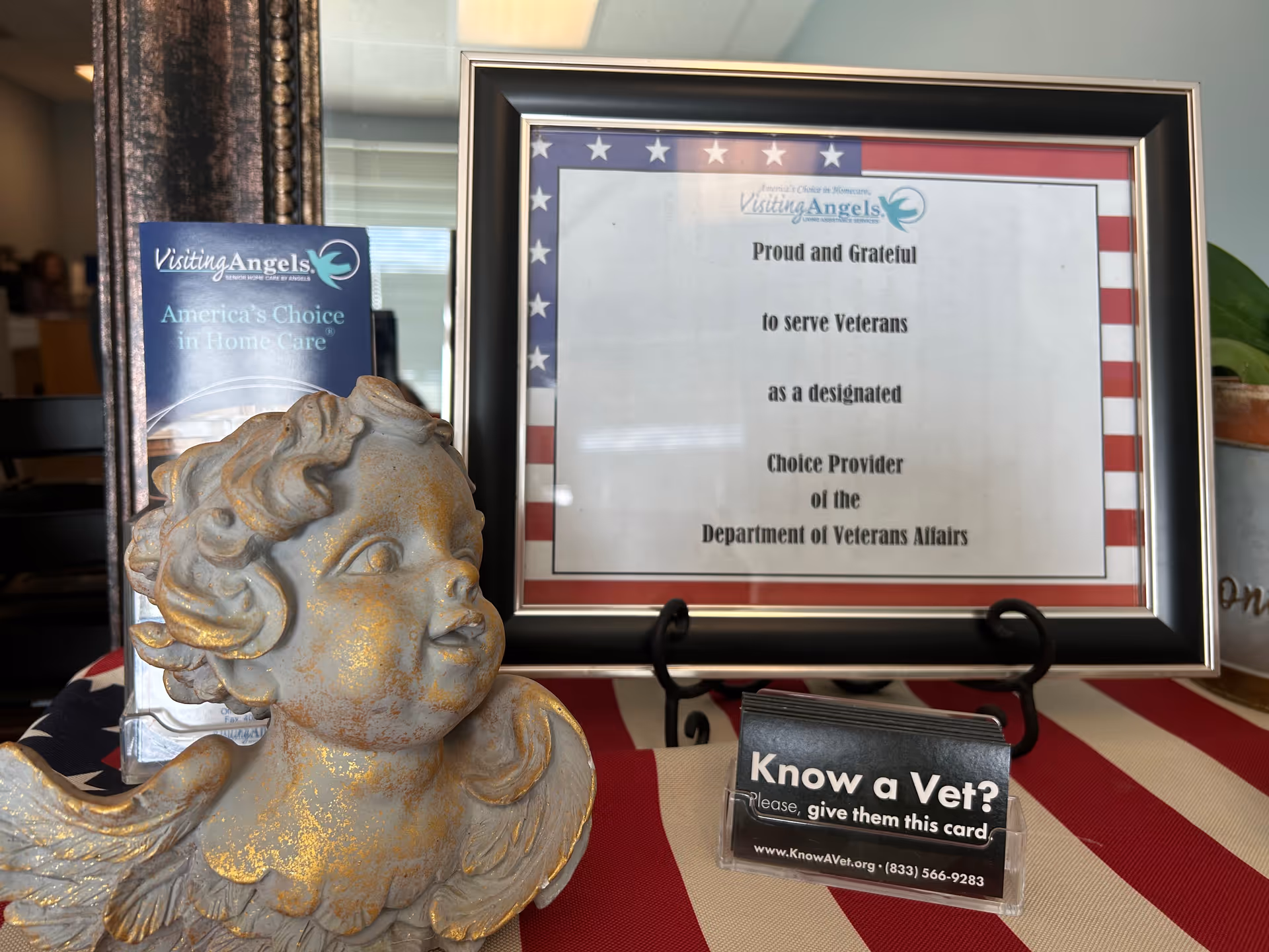 Framed certificate with patriotic border sits beside angel statue and brochures.