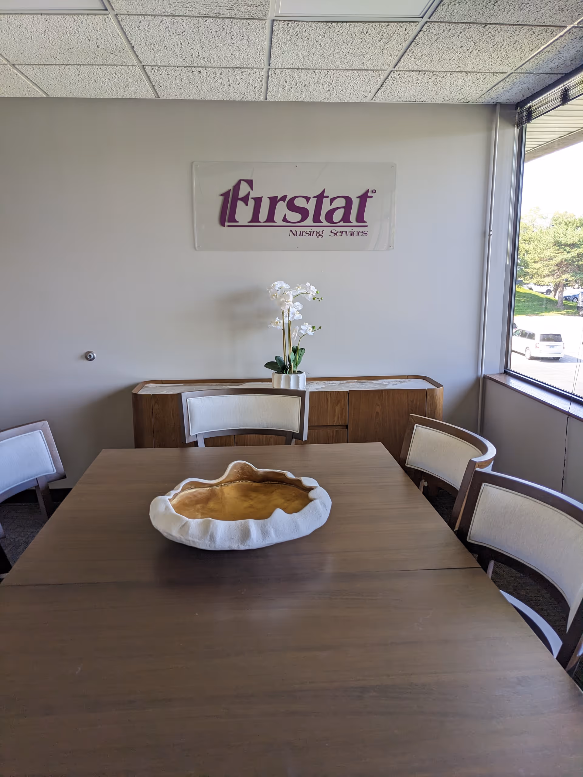 A dining room in a senior facility with a table, chairs, and Firstat Nursing Services sign.