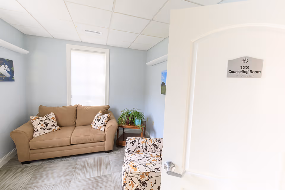 A beige sofa with floral cushions in a light blue lounge area beside a window.