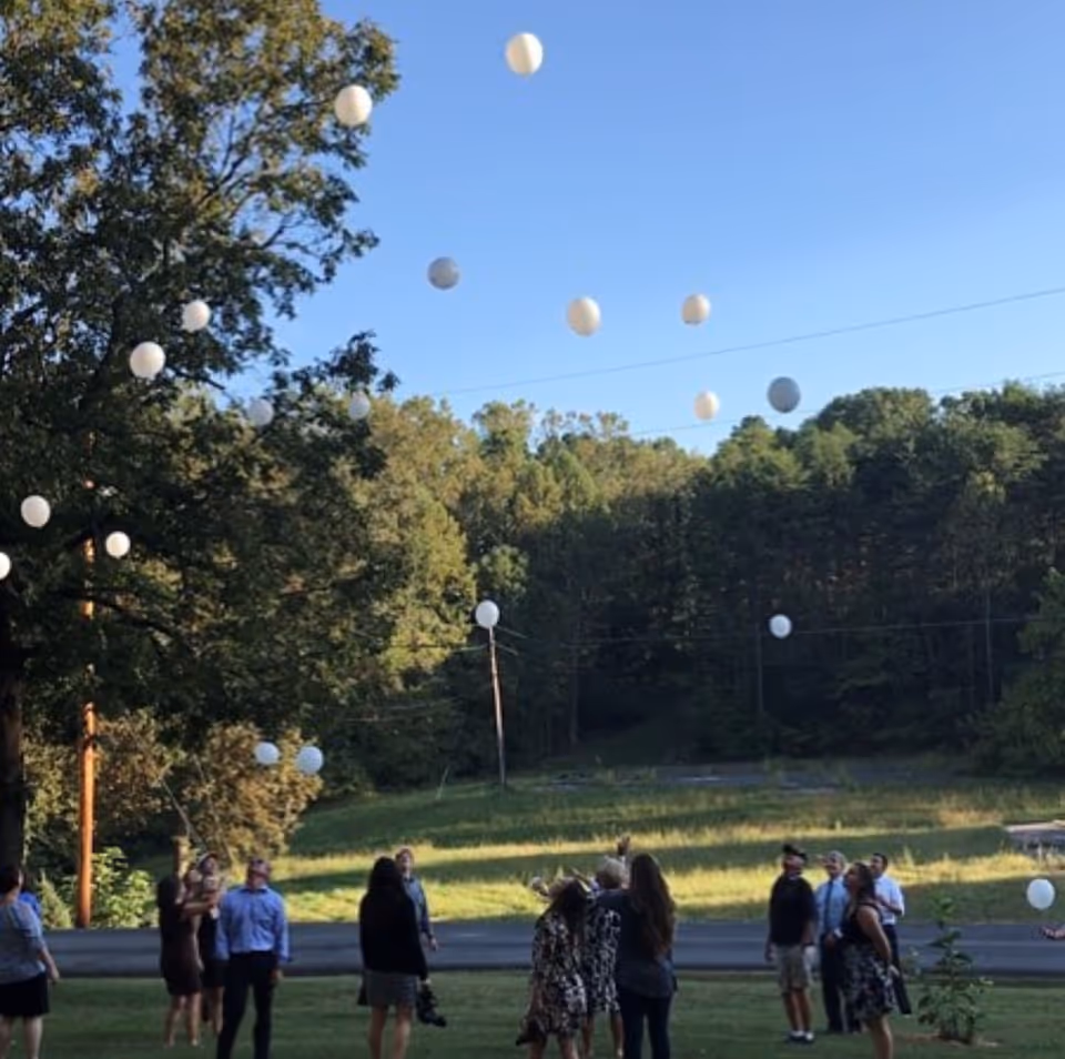 Groups of people release white balloons outdoors beneath a clear blue sky.