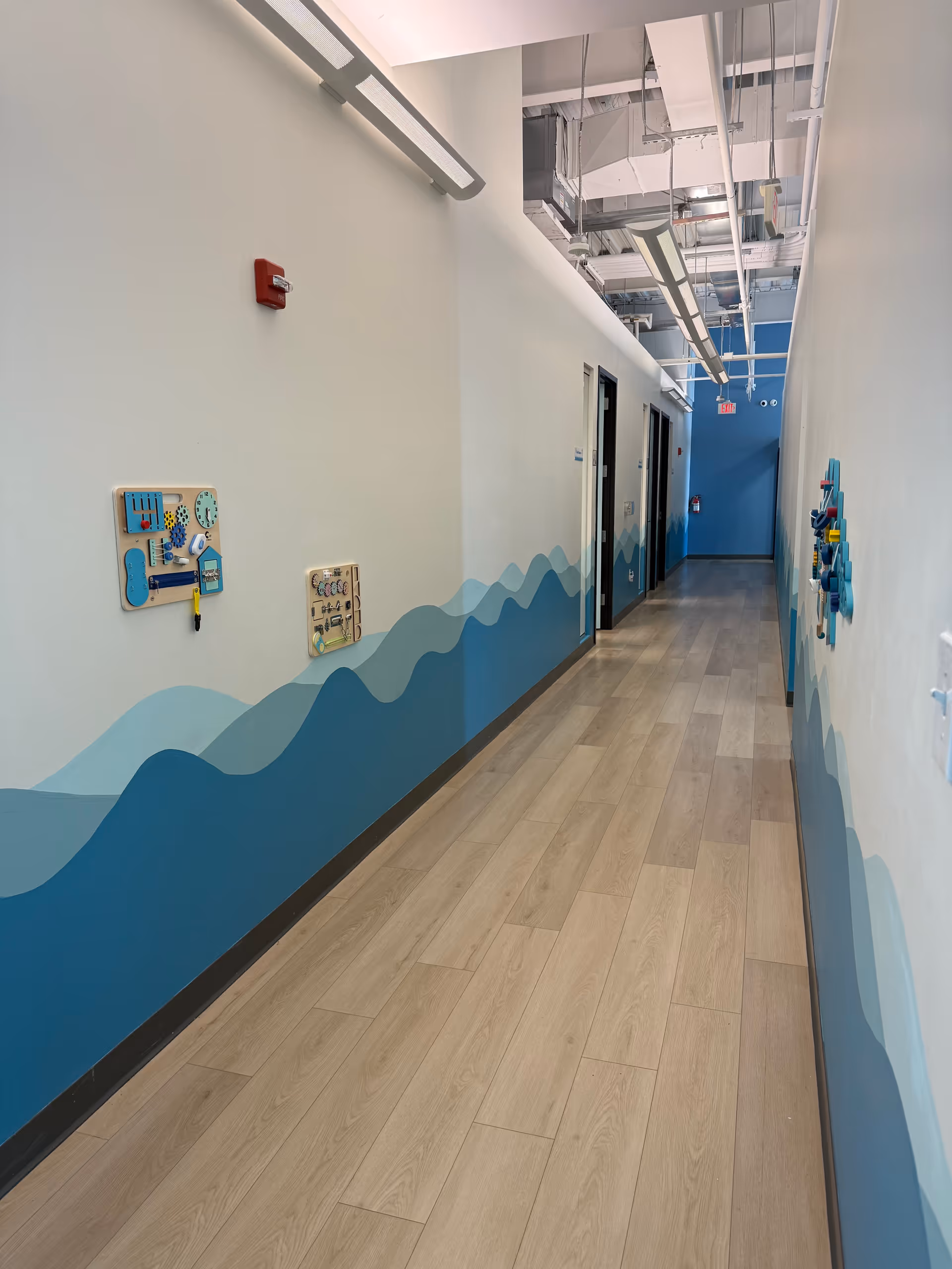 Long hallway inside a facility with wavy blue wall mural and ceiling fixtures.