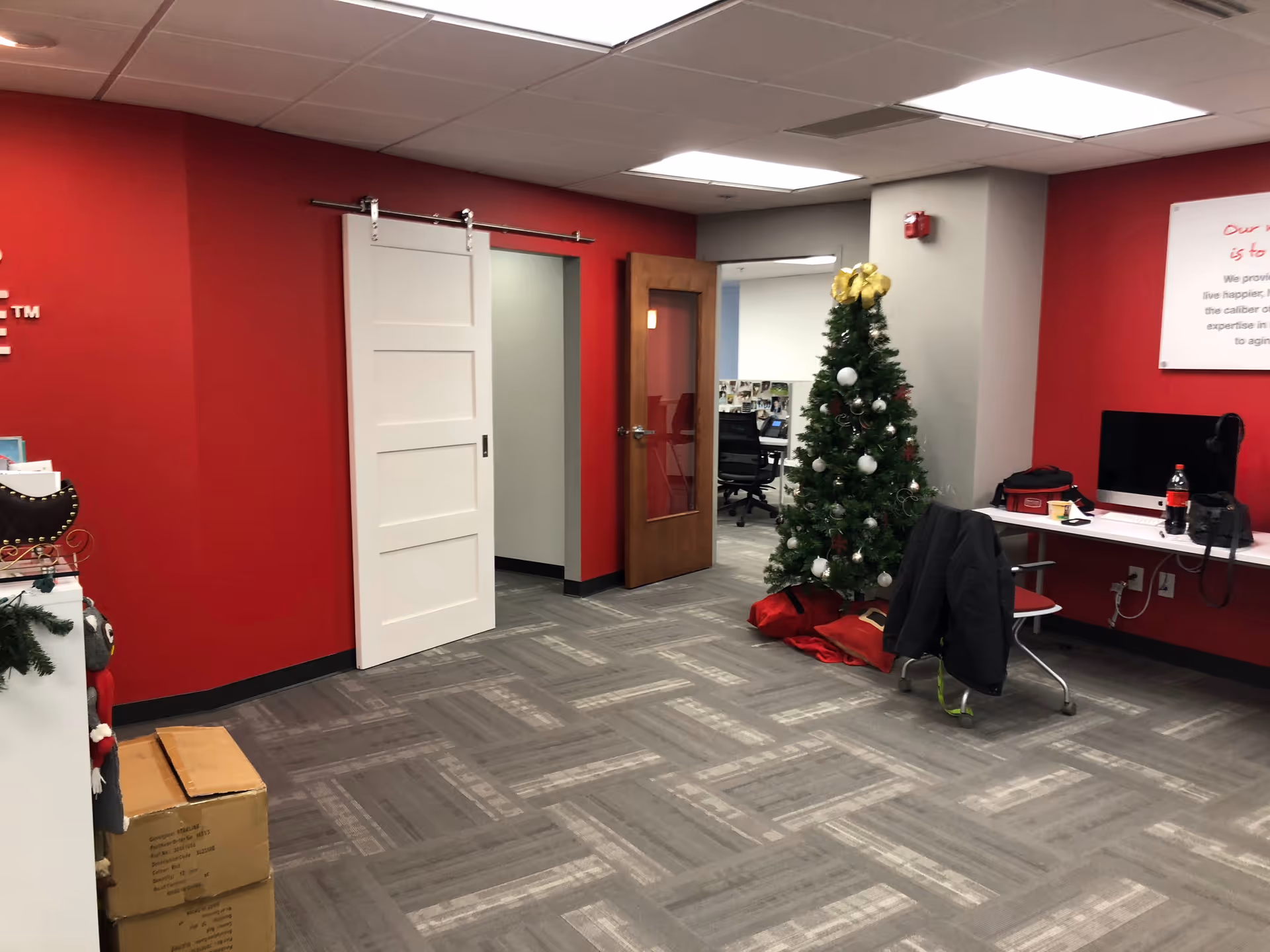 Red-walled office area with desks, a computer, and a decorated Christmas tree.