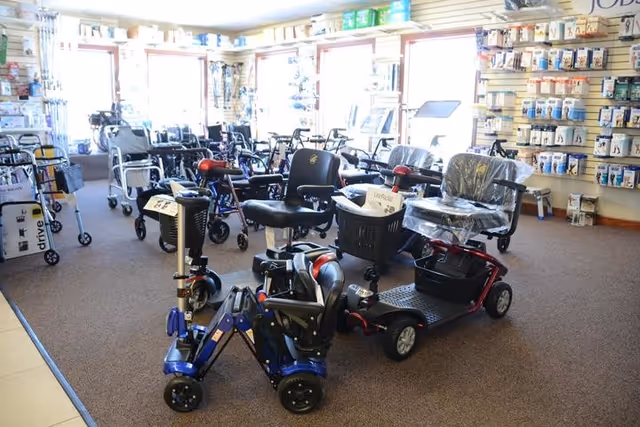 Indoor showroom with mobility aids—walkers, scooters, and wheelchairs arranged on a carpeted floor.