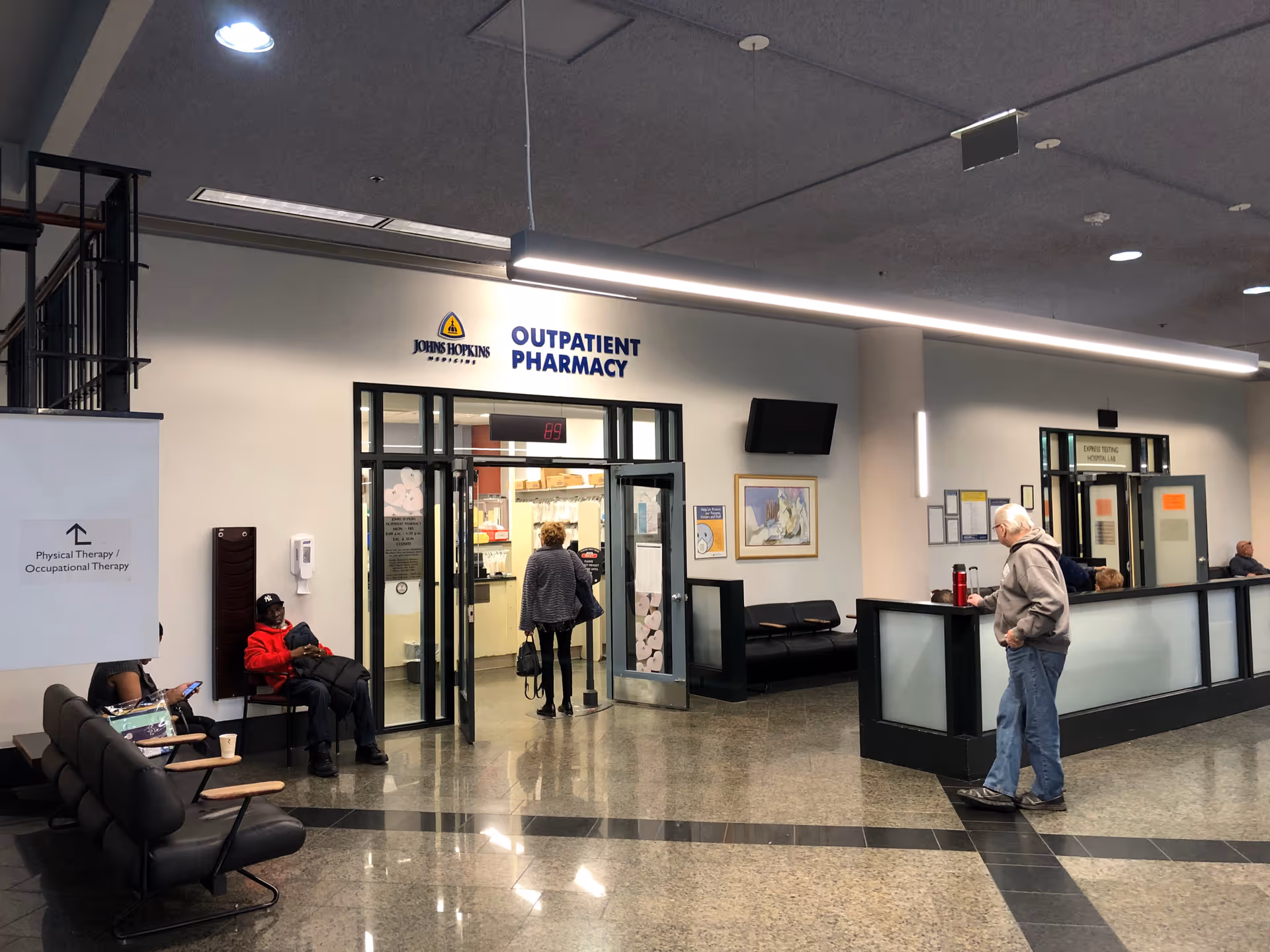 Interior view of Johns Hopkins Outpatient Pharmacy with seated visitors and a reception desk.