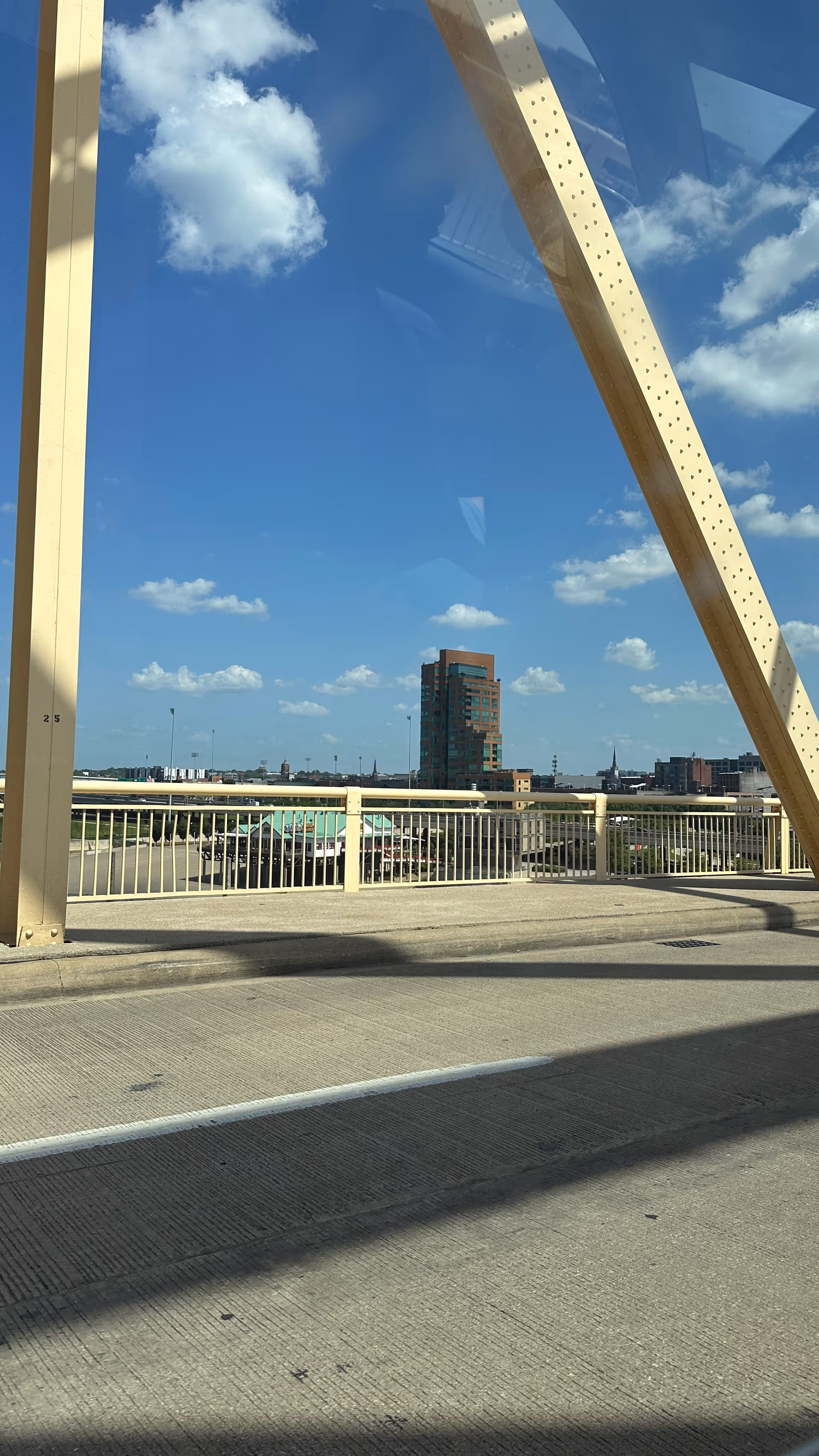 Beige steel bridge structure with railing and distant city skyline under blue sky.