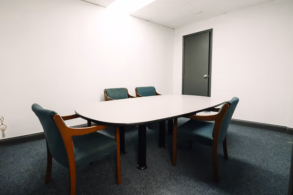 An empty dining room with a curved table and teal upholstered chairs.