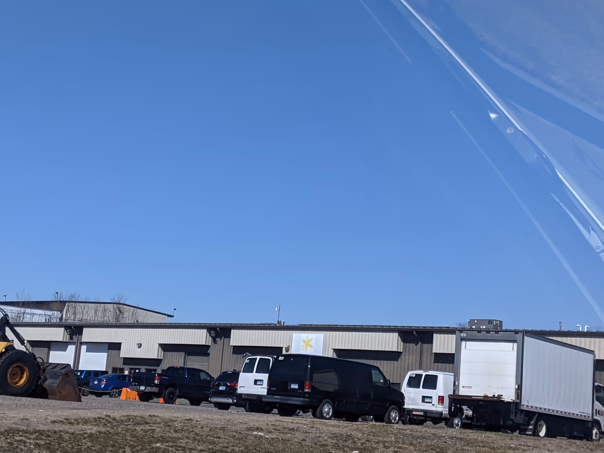 Exterior view of a warehouse-style facility with parked trucks and vans under a blue sky.