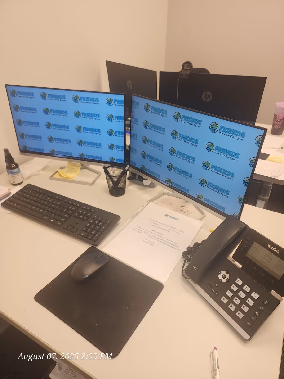 Office desk with dual monitors displaying Friends Home Health Agency branding, keyboard, mouse, and phone.