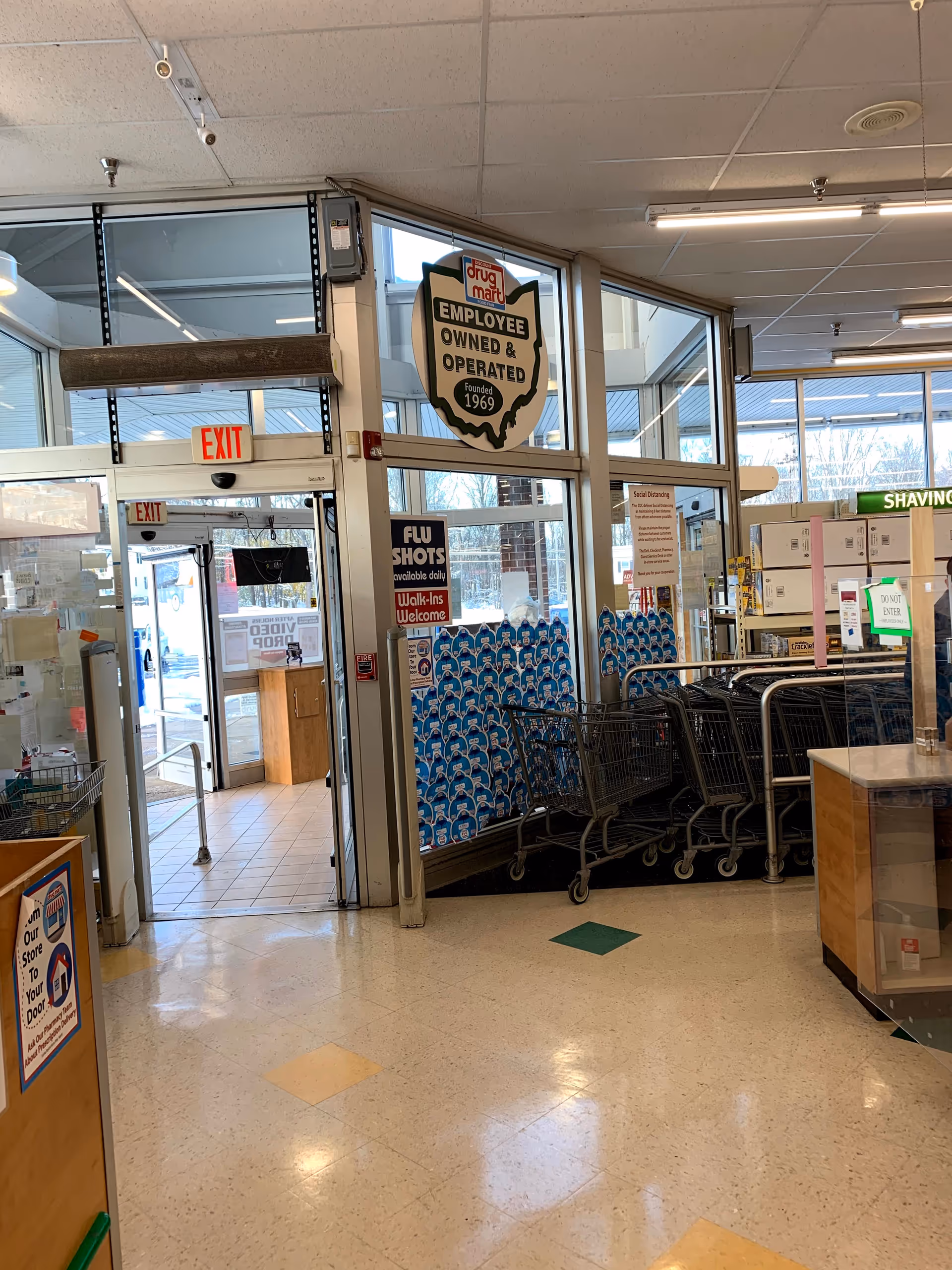 Inside a Discount Drug Mart store, shopping carts sit near glass doors and signage.