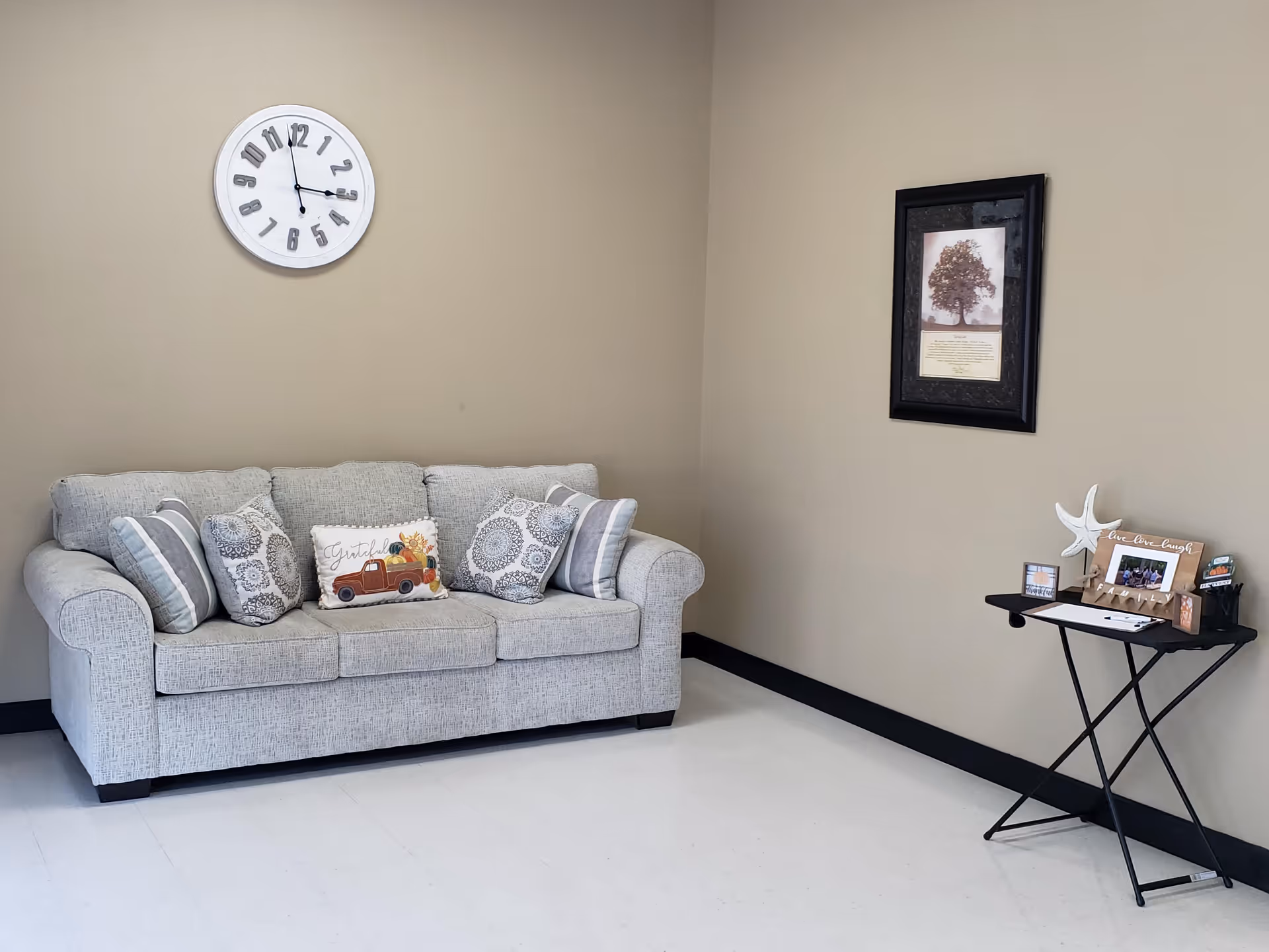 A light gray sofa with patterned cushions sits in a beige-walled living area with a clock.