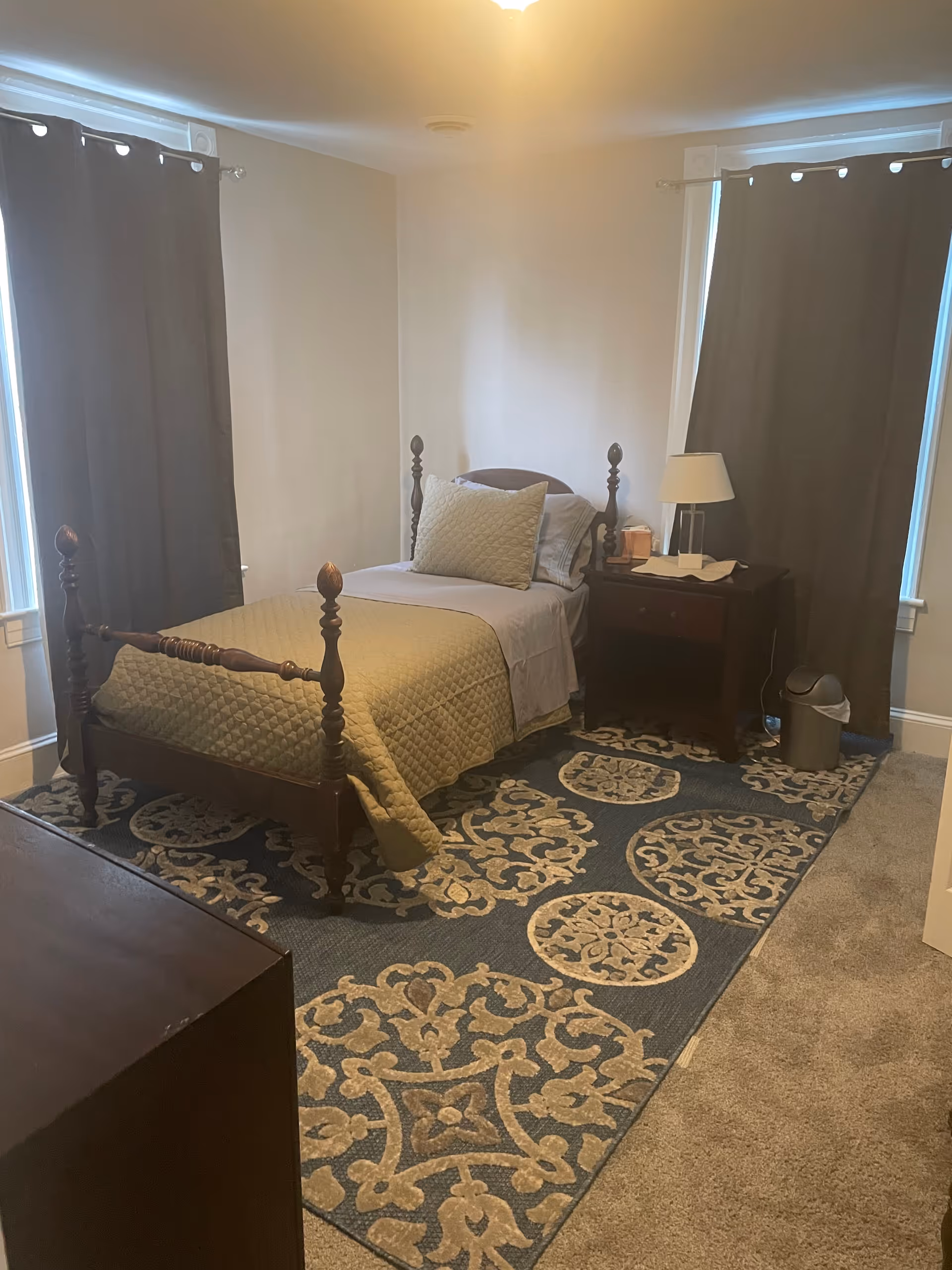 A furnished bedroom with a dark wood four-poster bed, nightstand, and curtains.